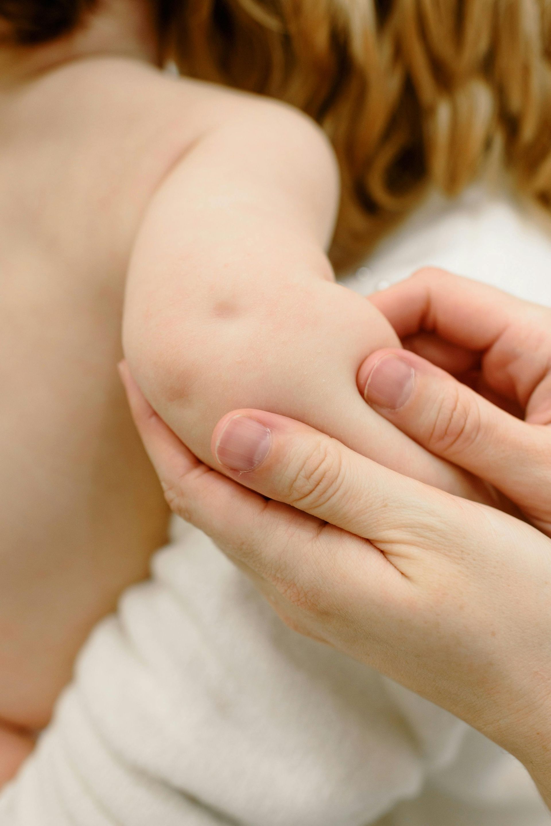 A person's hand gently holding a child's arm, focusing on the elbow.