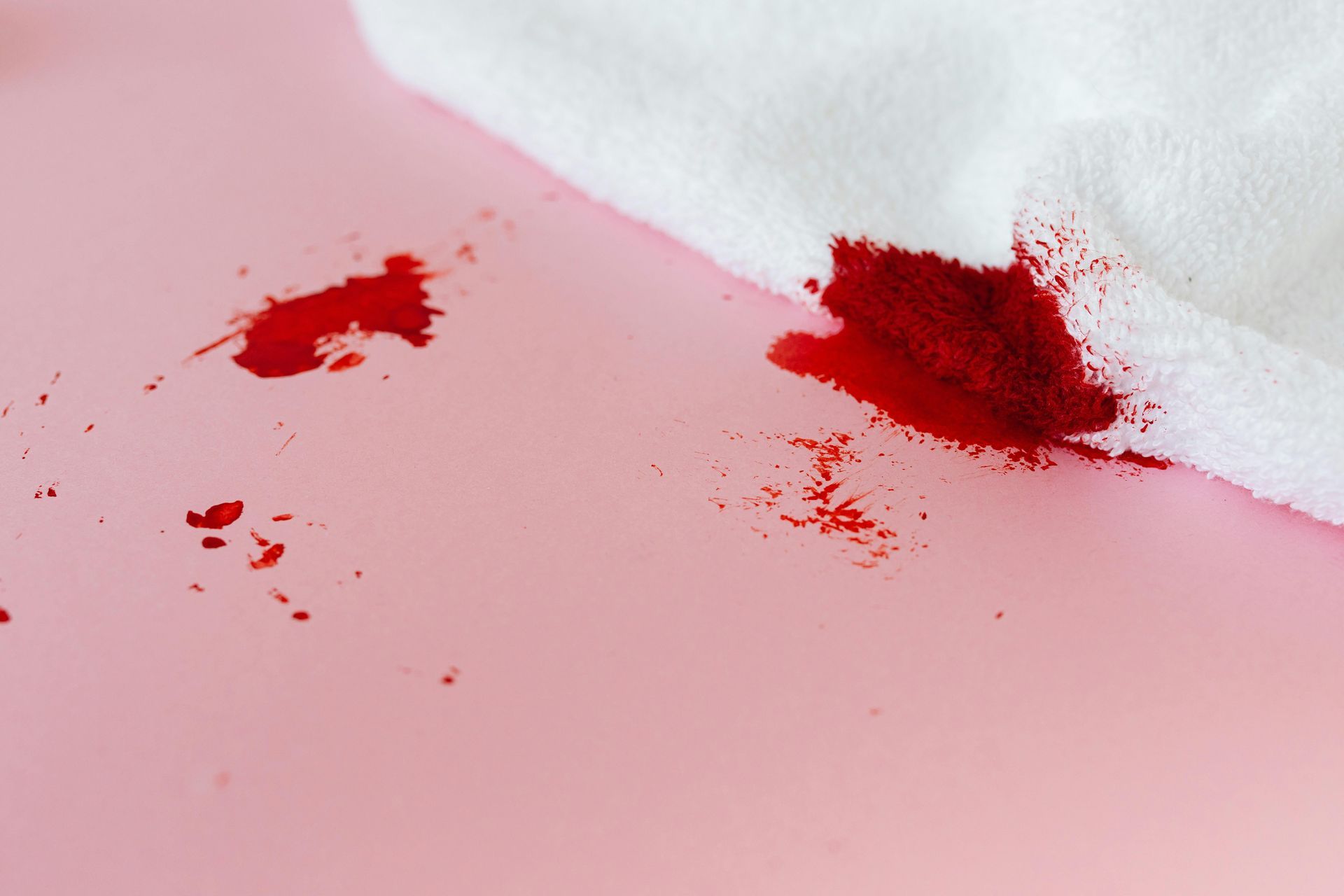 Bloodstained white cloth on a pink surface, with scattered blood droplets nearby.