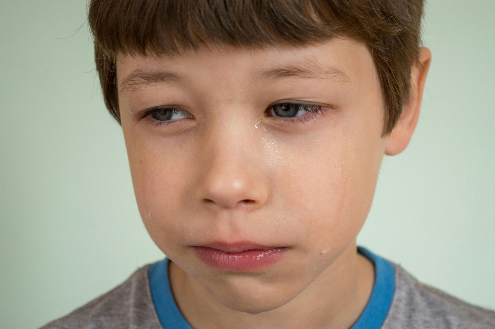Young boy with tear-stained cheeks, looking slightly away with a sad expression.