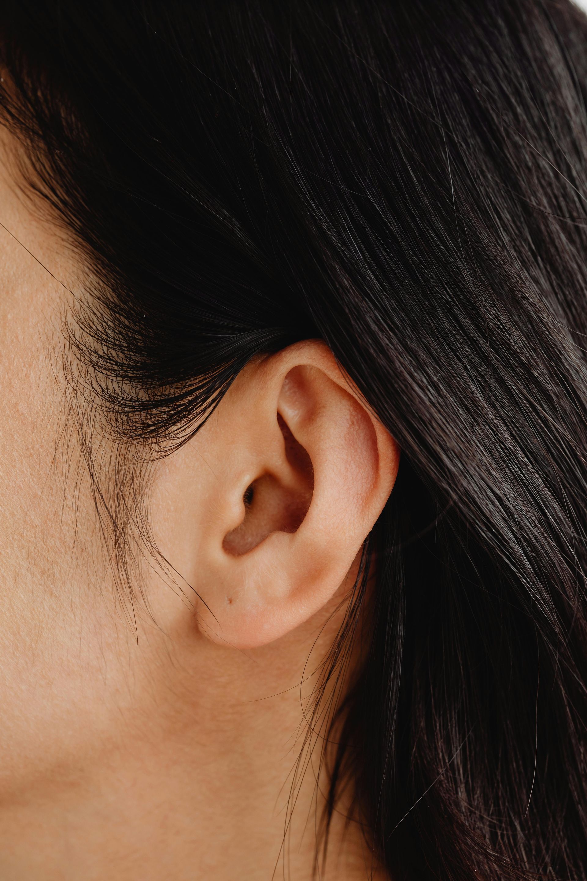 Close-up of a person's ear and dark hair. Skin is fair.