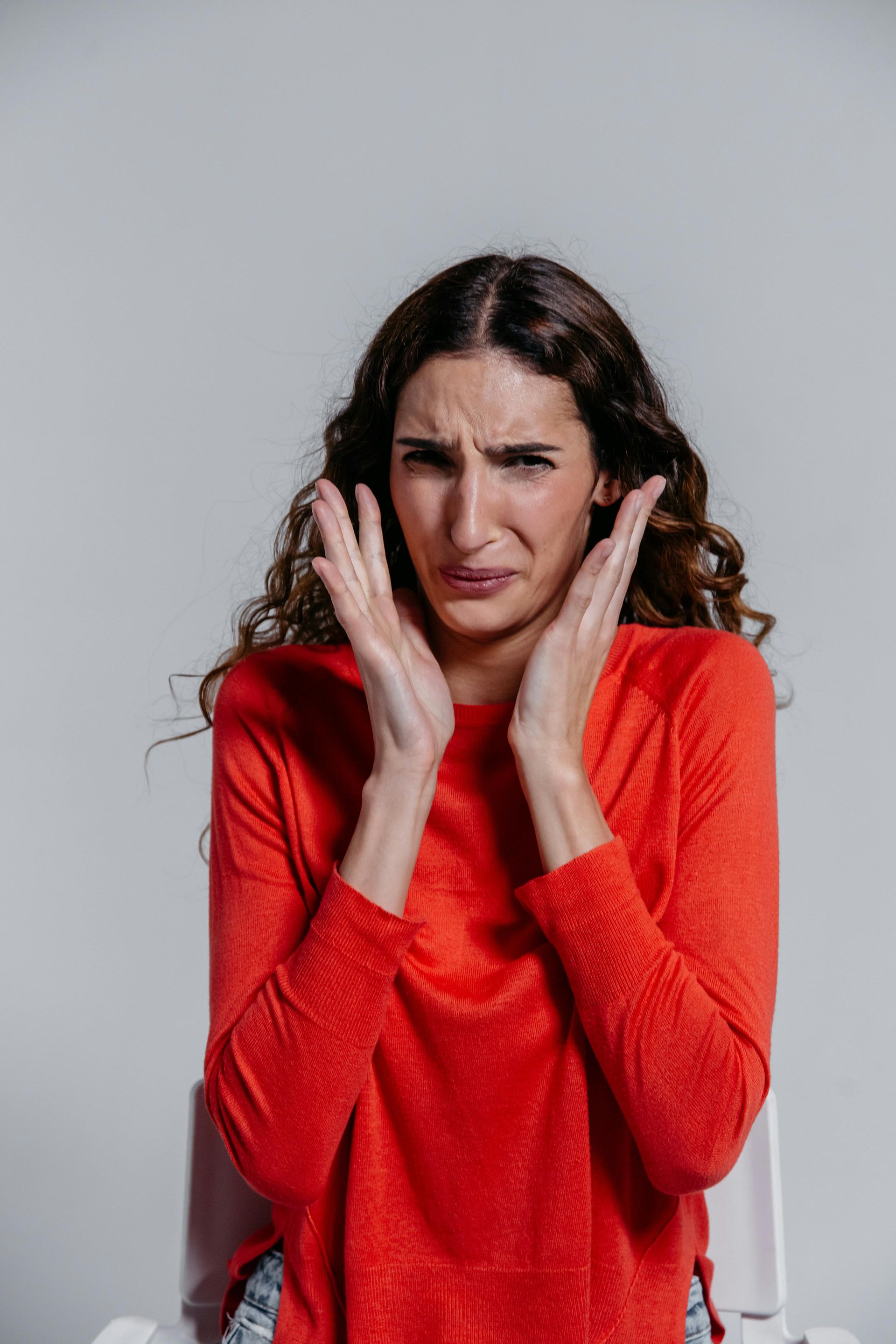 Woman in red shirt with hands on ears, grimacing in discomfort.