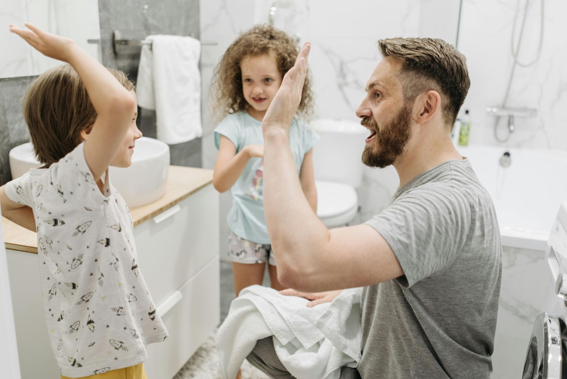 Father and two children in bathroom, high-fiving. Father is smiling, children are smiling.