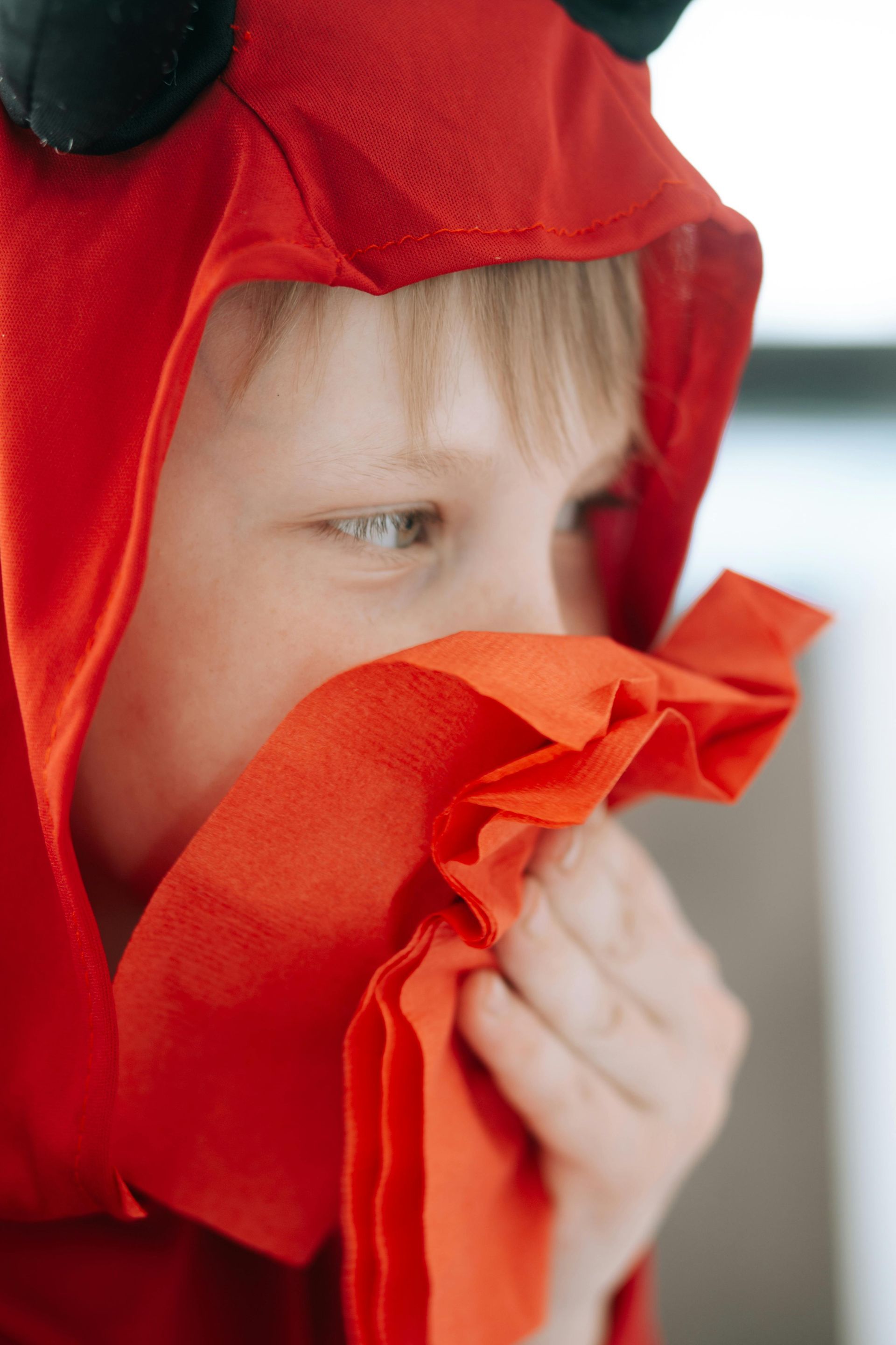 Boy in red devil costume blowing his nose with a red tissue.