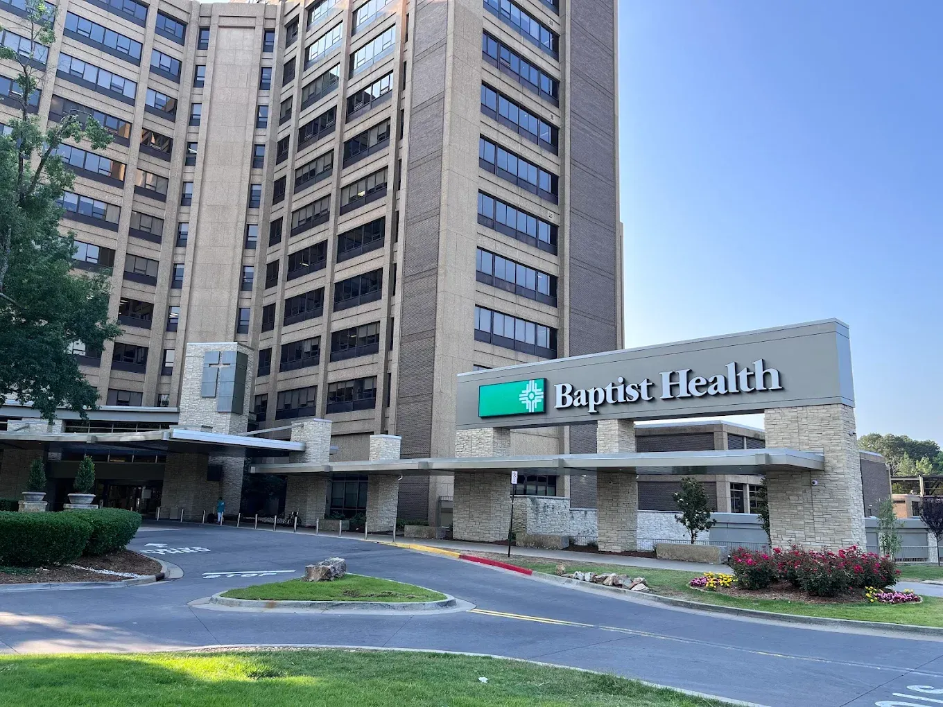 Baptist Health hospital exterior with sign and high-rise building under blue sky.