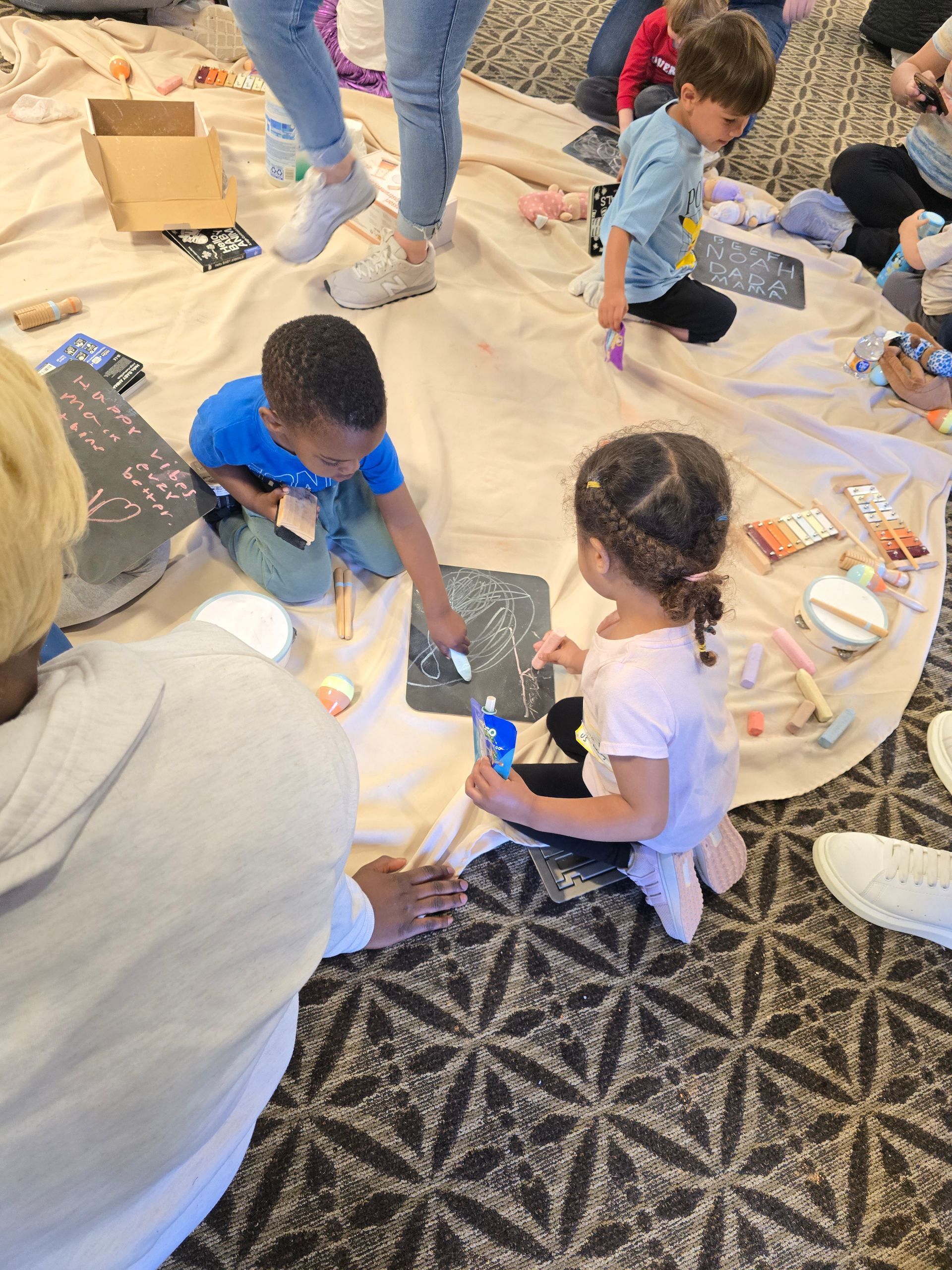 Children sitting on a patterned rug doing a craft activity with paper and supplies
