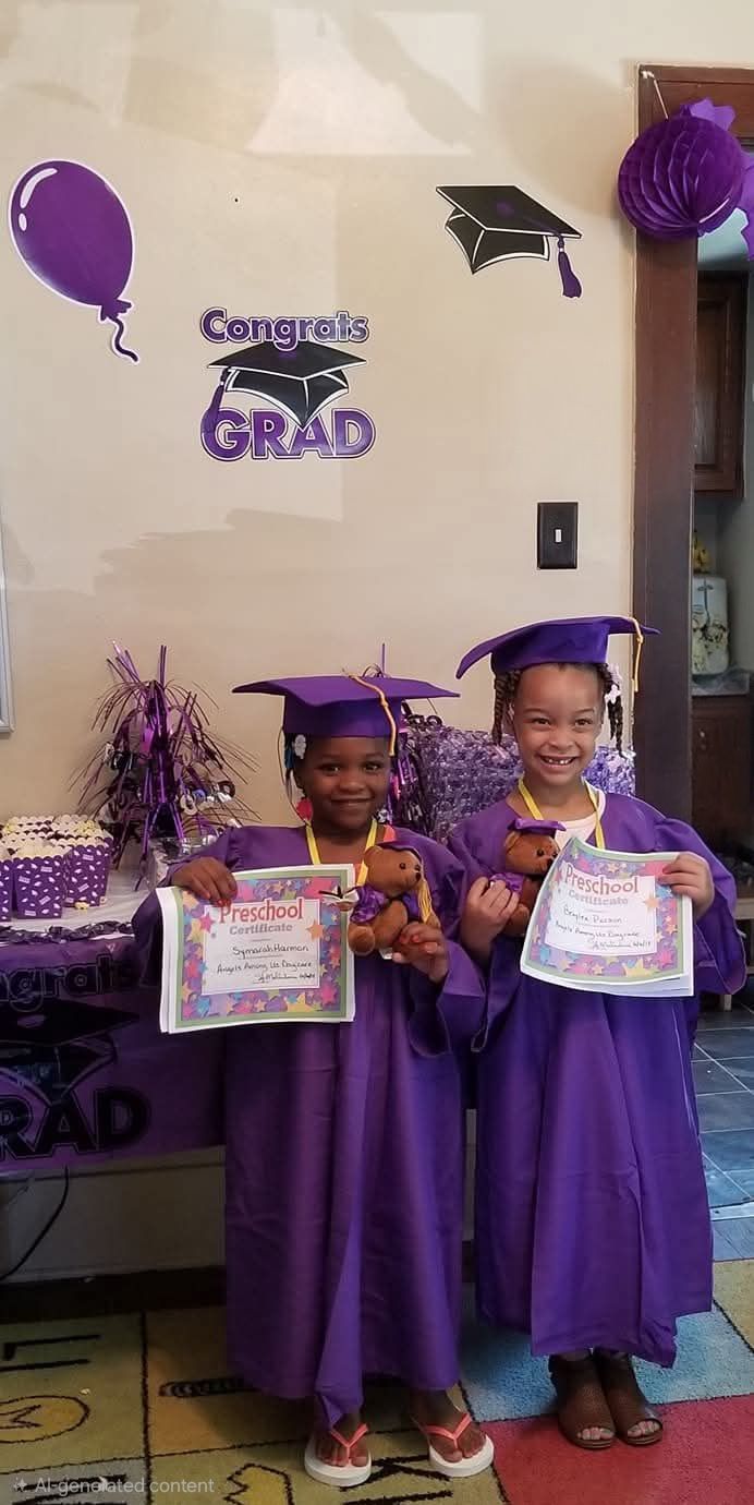 Two children in purple graduation gowns hold certificates in a decorated school celebration area.