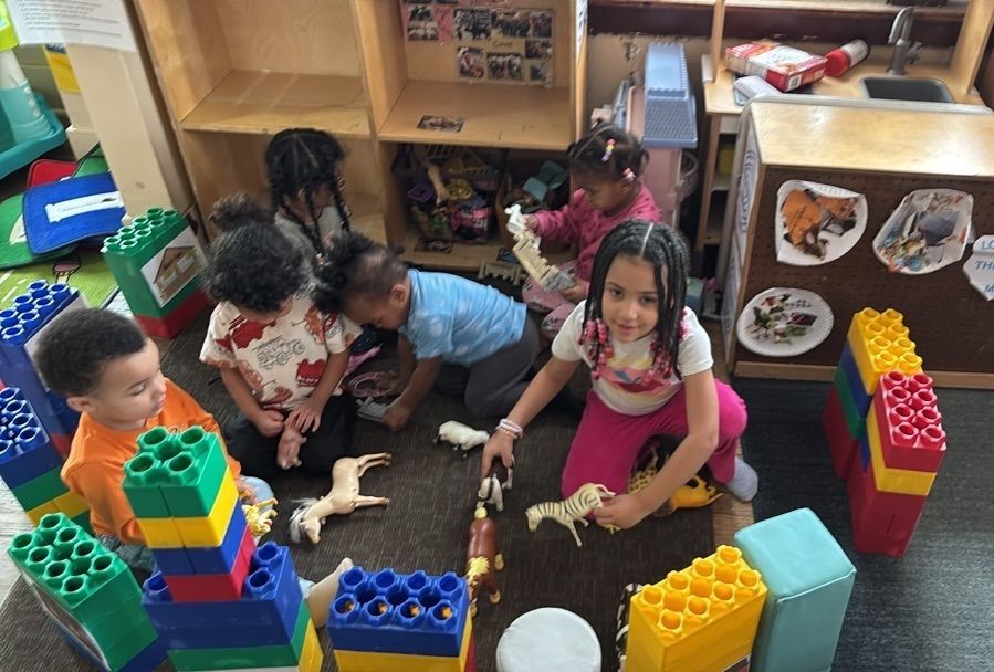 Children sitting on a classroom floor playing with colorful building blocks and toy animals