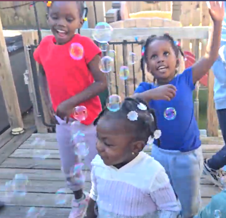 Three children playing with bubbles on a wooden deck outdoors