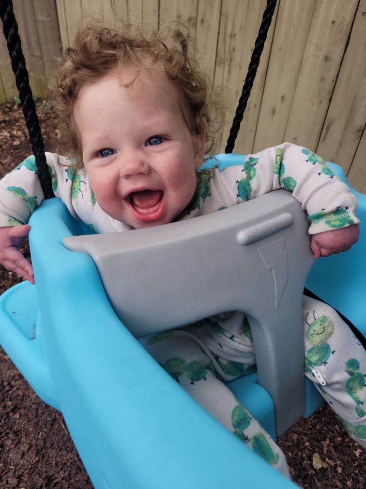 Smiling child in a gray and blue swing, reaching forward outdoors