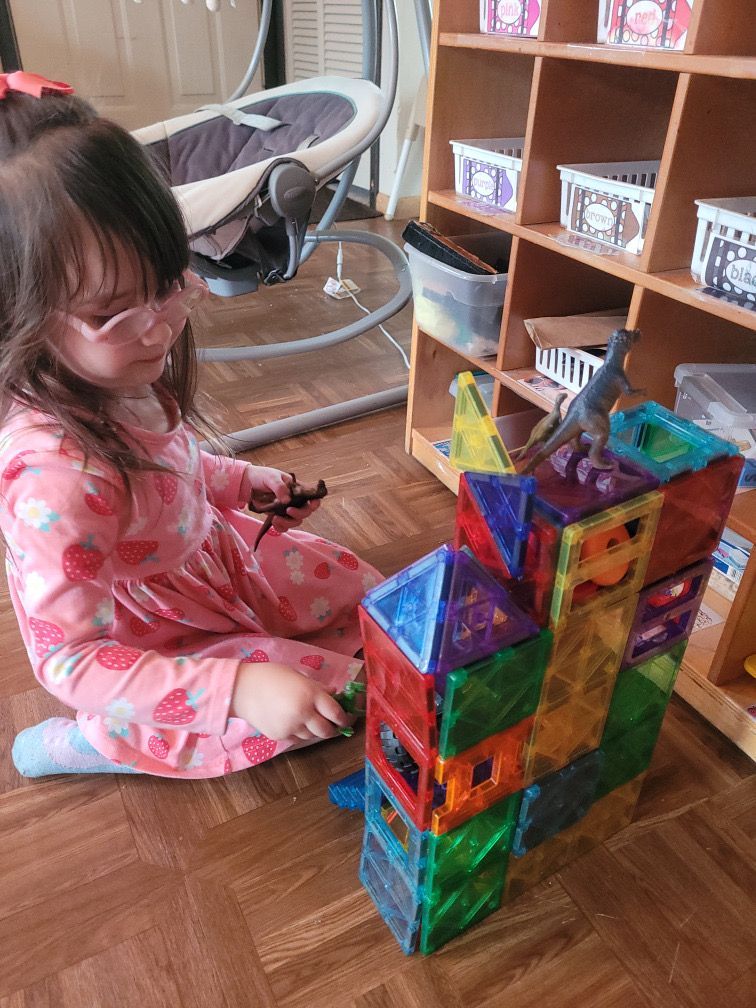 Child building a colorful block tower on a wooden floor in a living room.