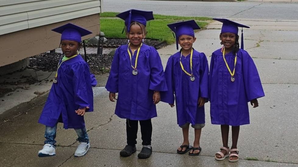 Four children in purple graduation caps and gowns walking together outdoors