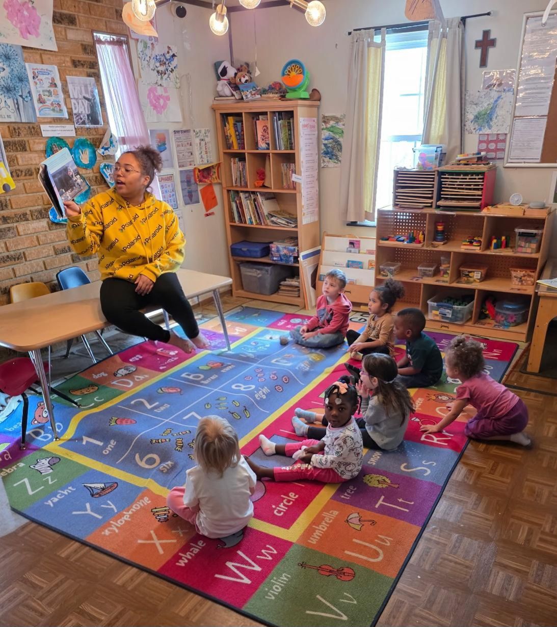 Teacher reading to children on a colorful rug in a classroom, with toys and bookshelves around them