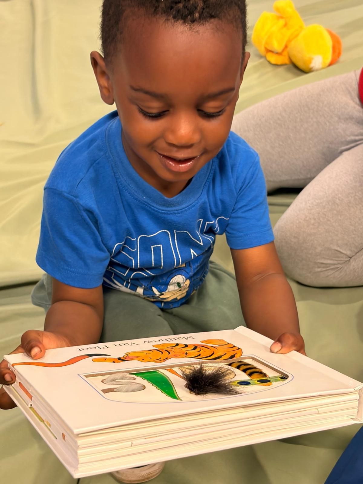Child smiling while looking at an open book on a couch, holding the book with both hands.
