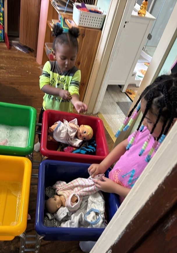 Children playing with dolls in colorful bins in a classroom.