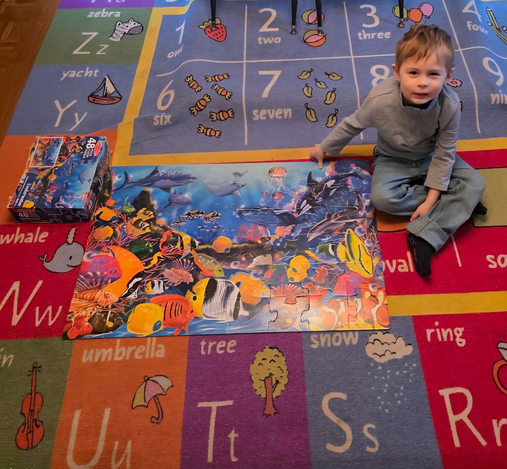 Child sitting on a colorful alphabet play mat with a large world map puzzle in the center