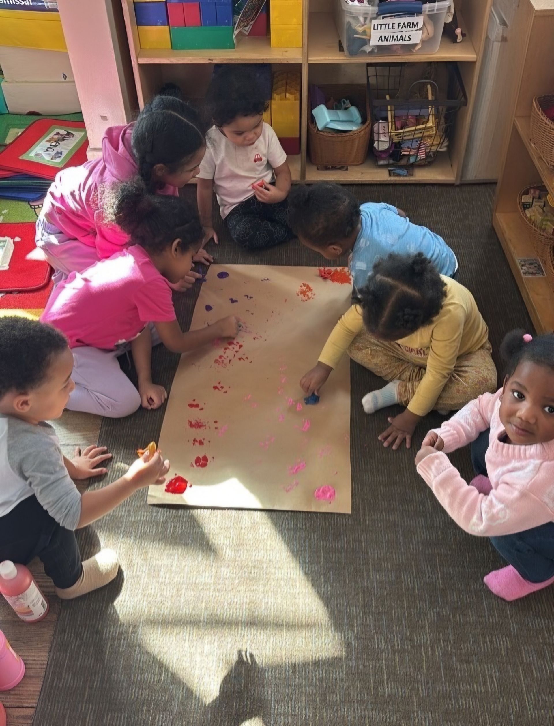 Five children sit at a table in a bright room, smiling while playing with colorful modeling clay.