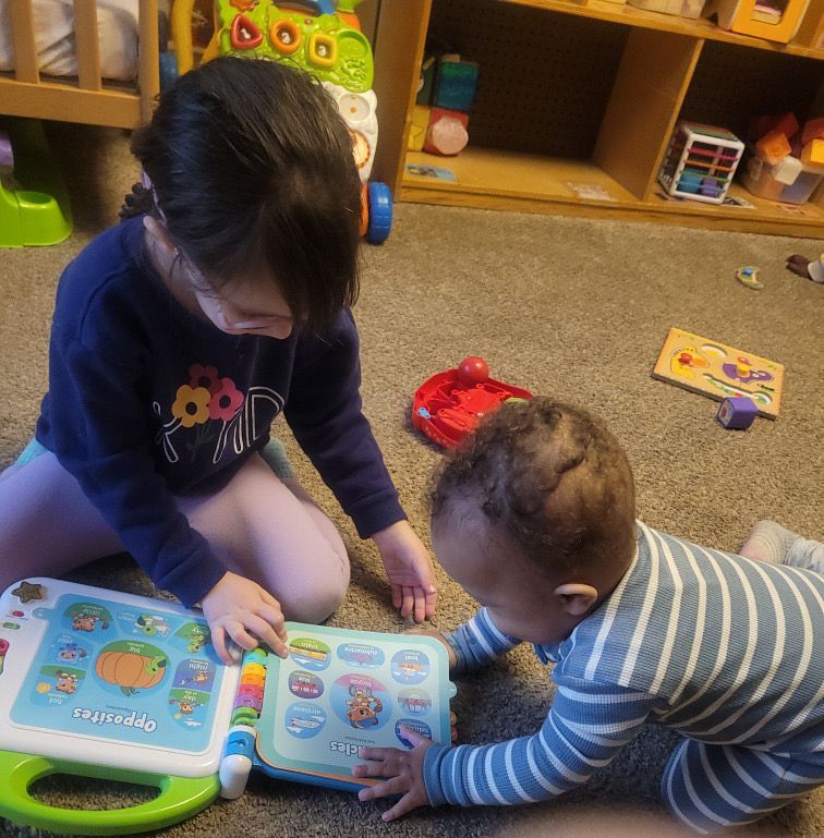 Two children sit on a carpet reading a colorful interactive book together.