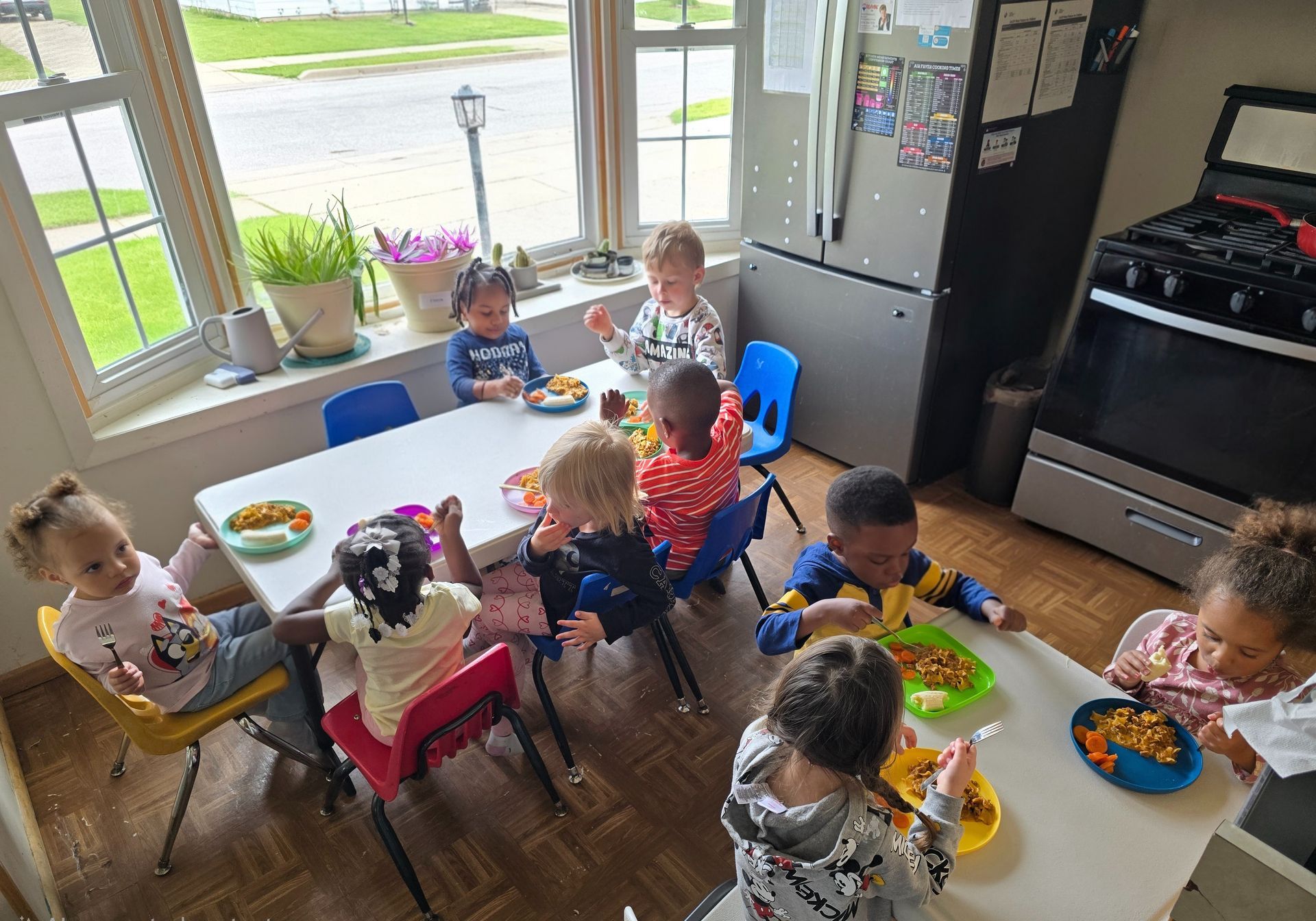 A smiling child sits at a table in a classroom, holding a yellow apple with various fruits nearby.
