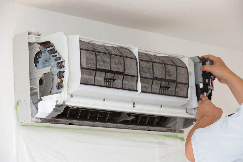 Person cleaning a dirty air conditioner, removing filters in a bright room— Lit Energy in Marian, QLD