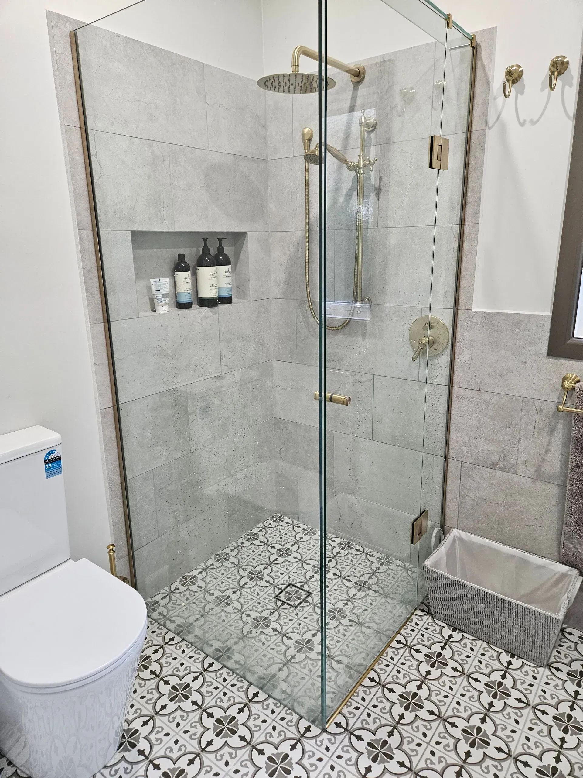 Modern bathroom with glass shower enclosure, patterned tile floor, toilet, and wall niche