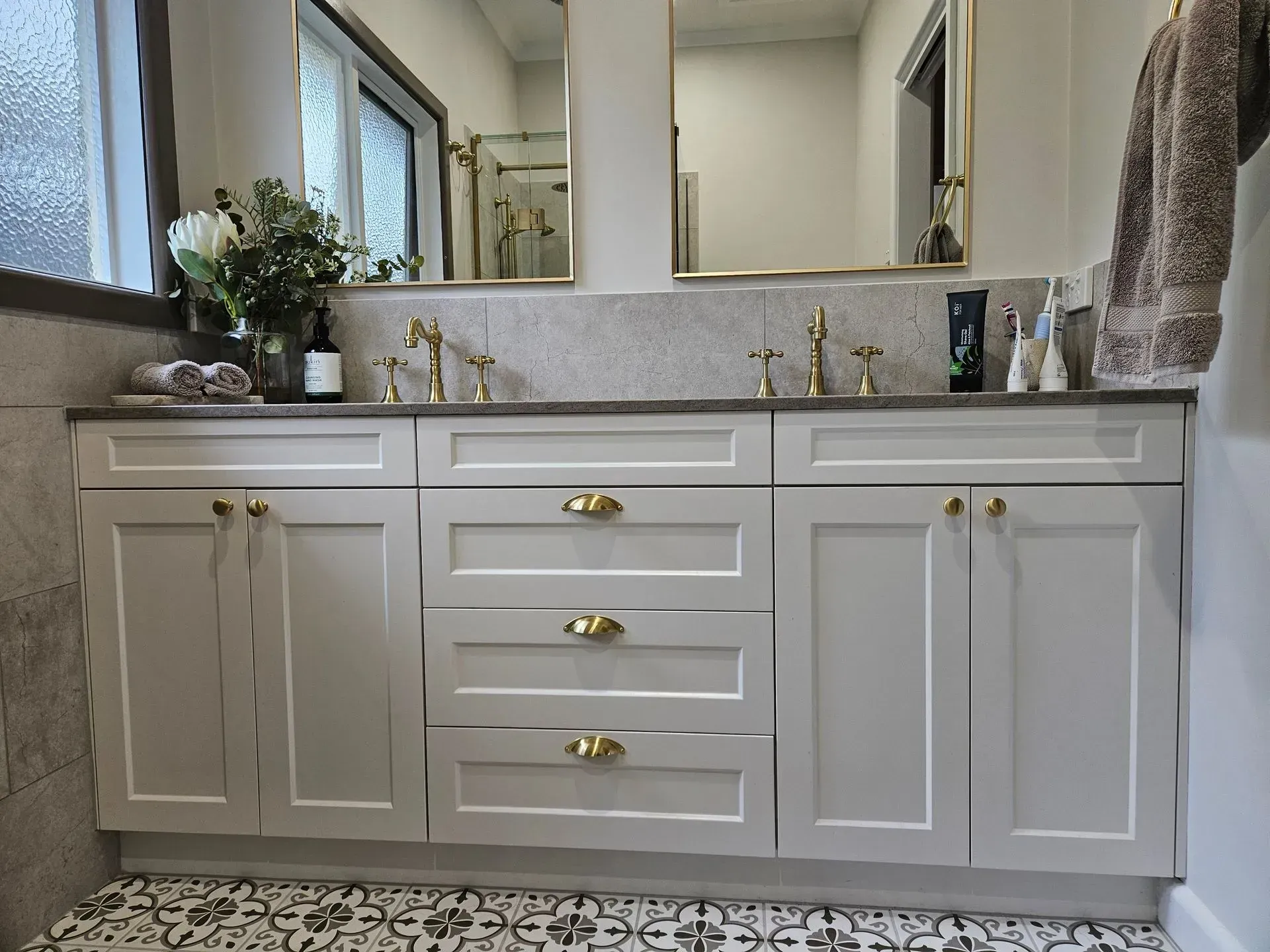 Bathroom vanity with gray cabinets, brass hardware, double sinks, and a large mirror above a marble countertop