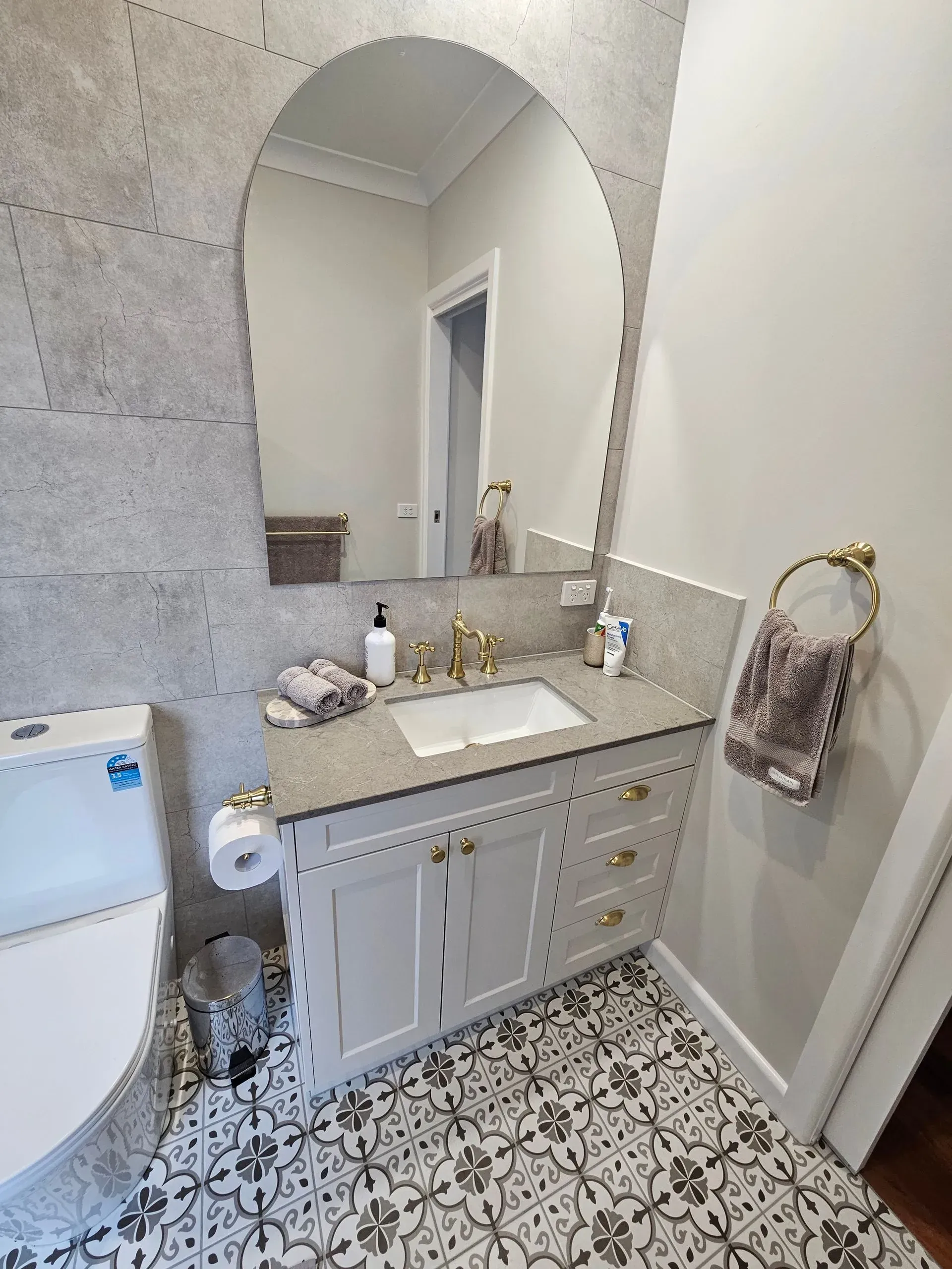 Bathroom vanity with oval mirror, marble countertop, and patterned tile floor
