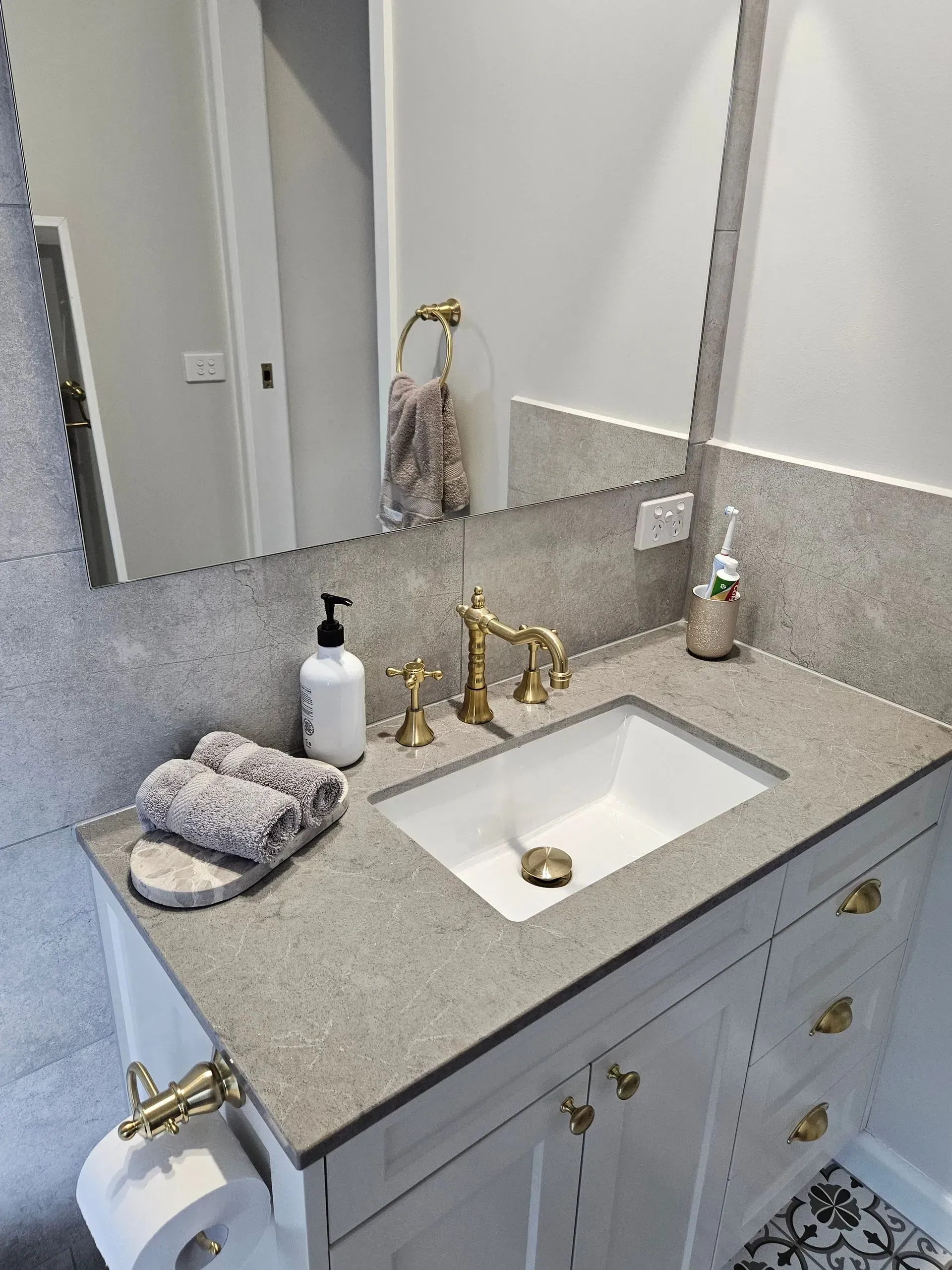 Bathroom vanity with gold faucet, white sink, large mirror, soap dispenser, and folded towels