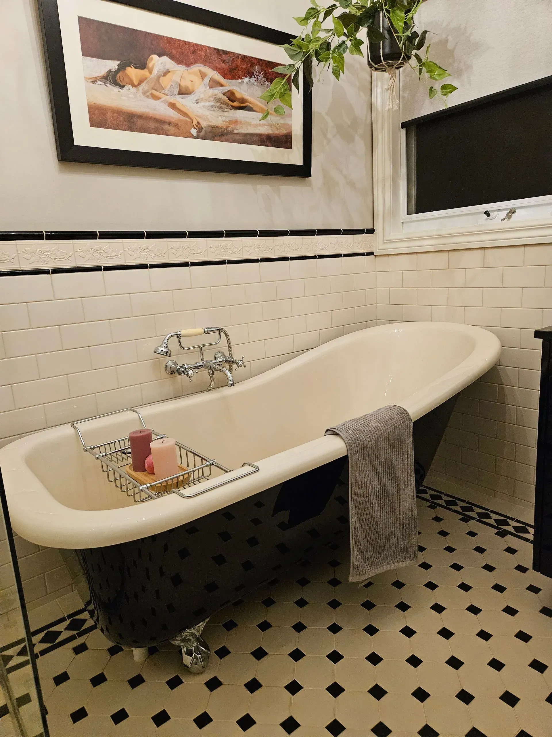 Vintage clawfoot bathtub in a tiled bathroom with a towel and framed wall art.