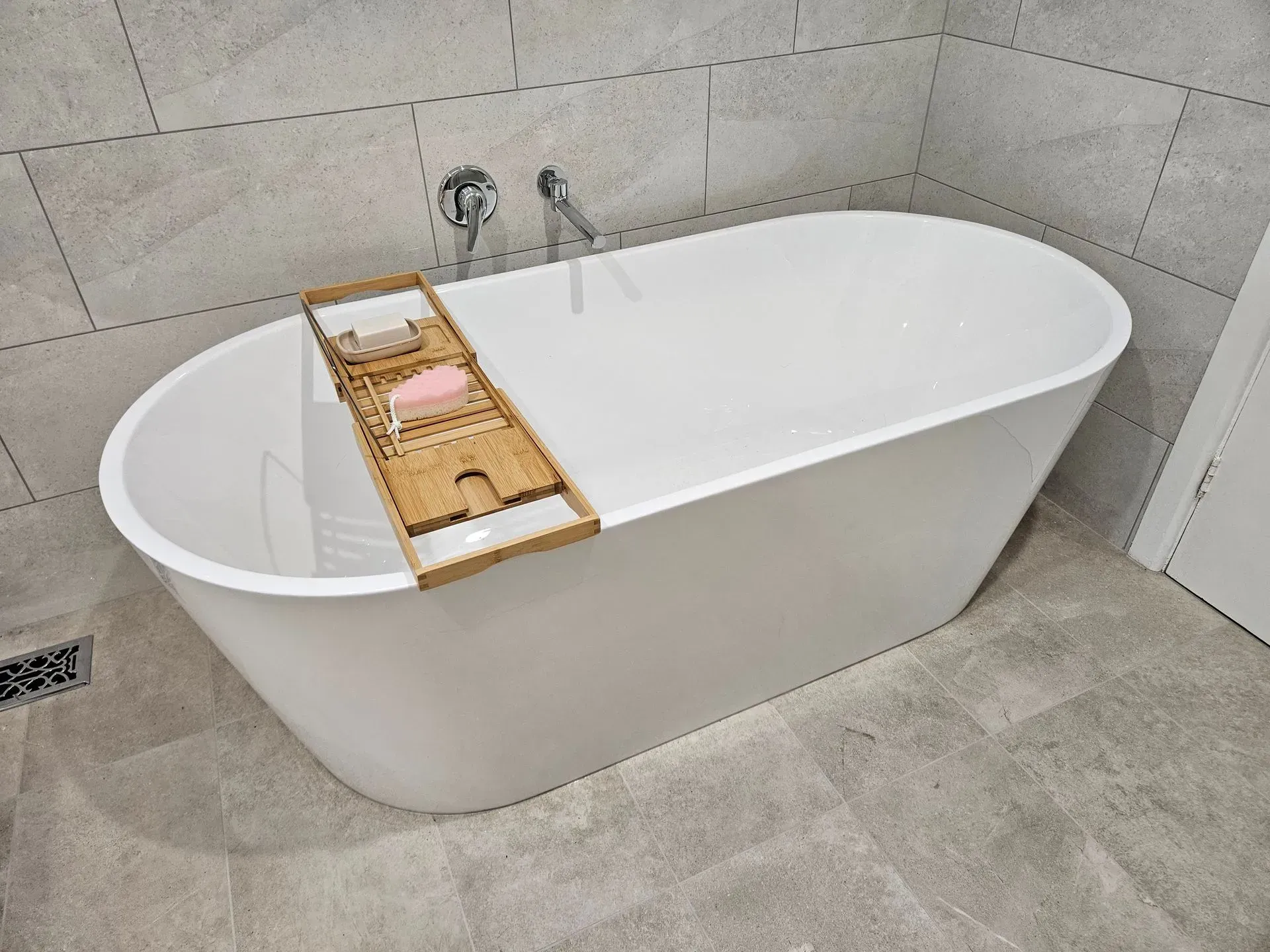 White freestanding bathtub with a wooden bath tray in a tiled bathroom