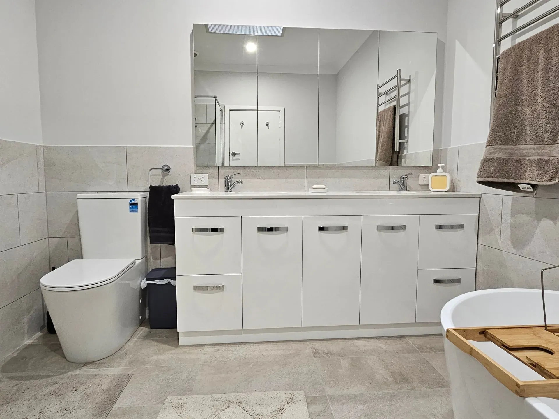 Modern bathroom with white vanity, large mirror, toilet, and bathtub under a window