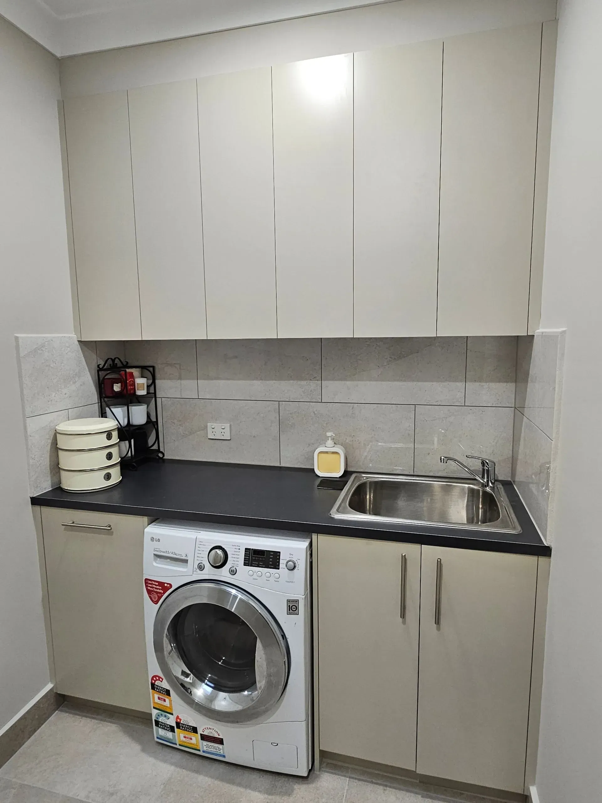 Small kitchen with white cabinets, gray countertop, sink, and a front-loading washing machine under the counter