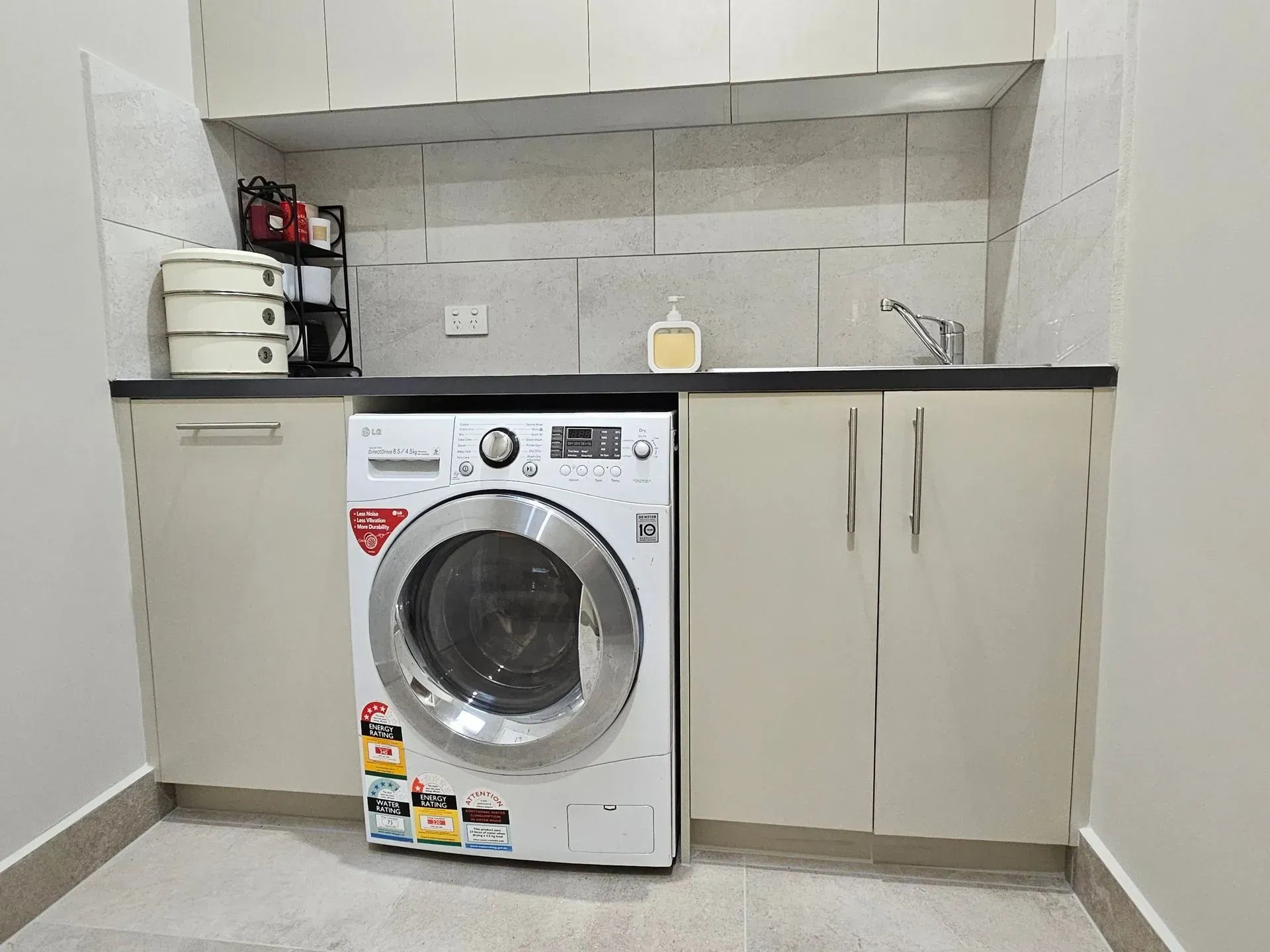 Laundry room with front-loading washer, beige cabinets, black countertop, and tiled walls