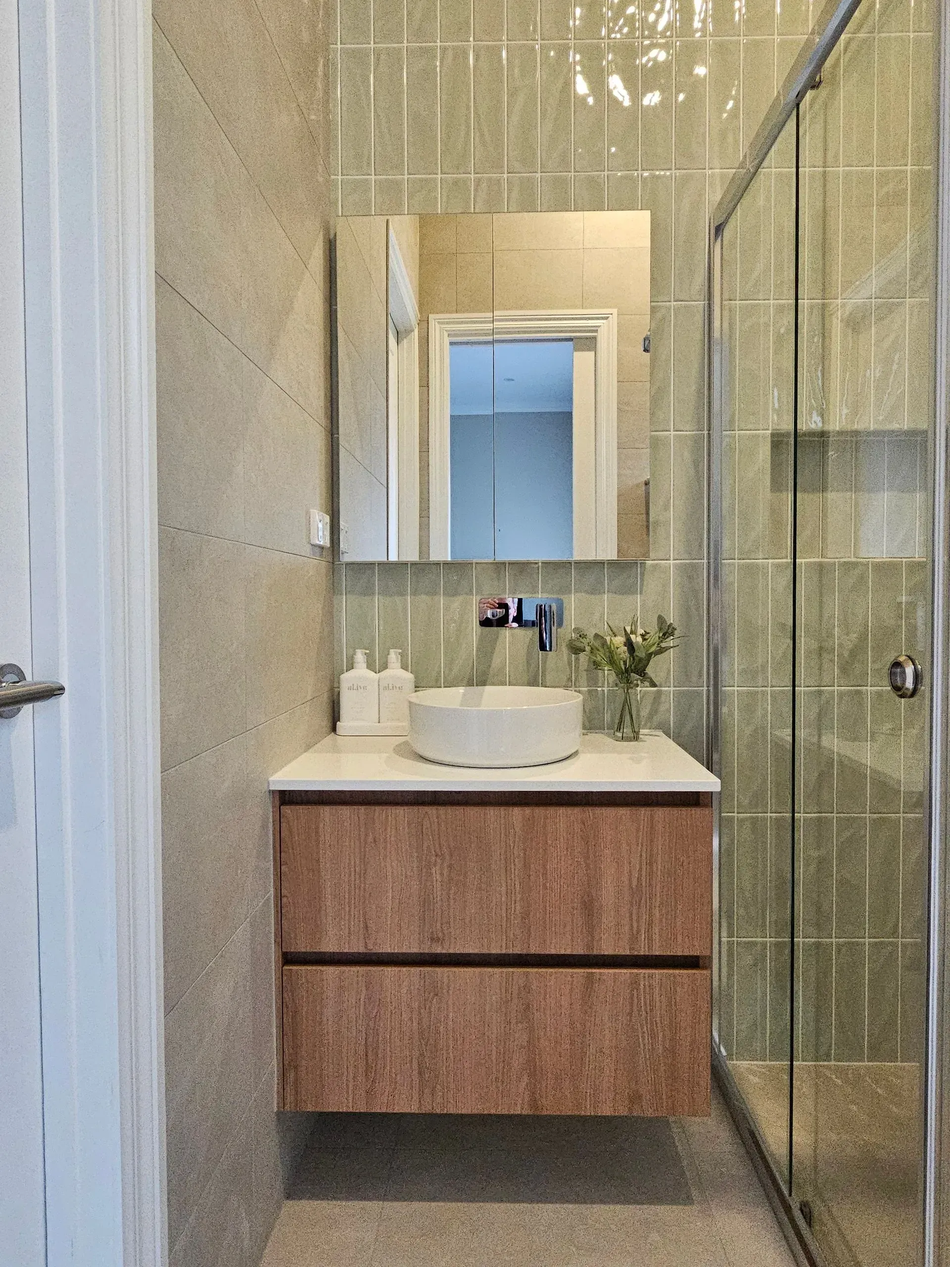 Modern bathroom vanity with mirror, white sink, and glass shower enclosure in a narrow tiled space