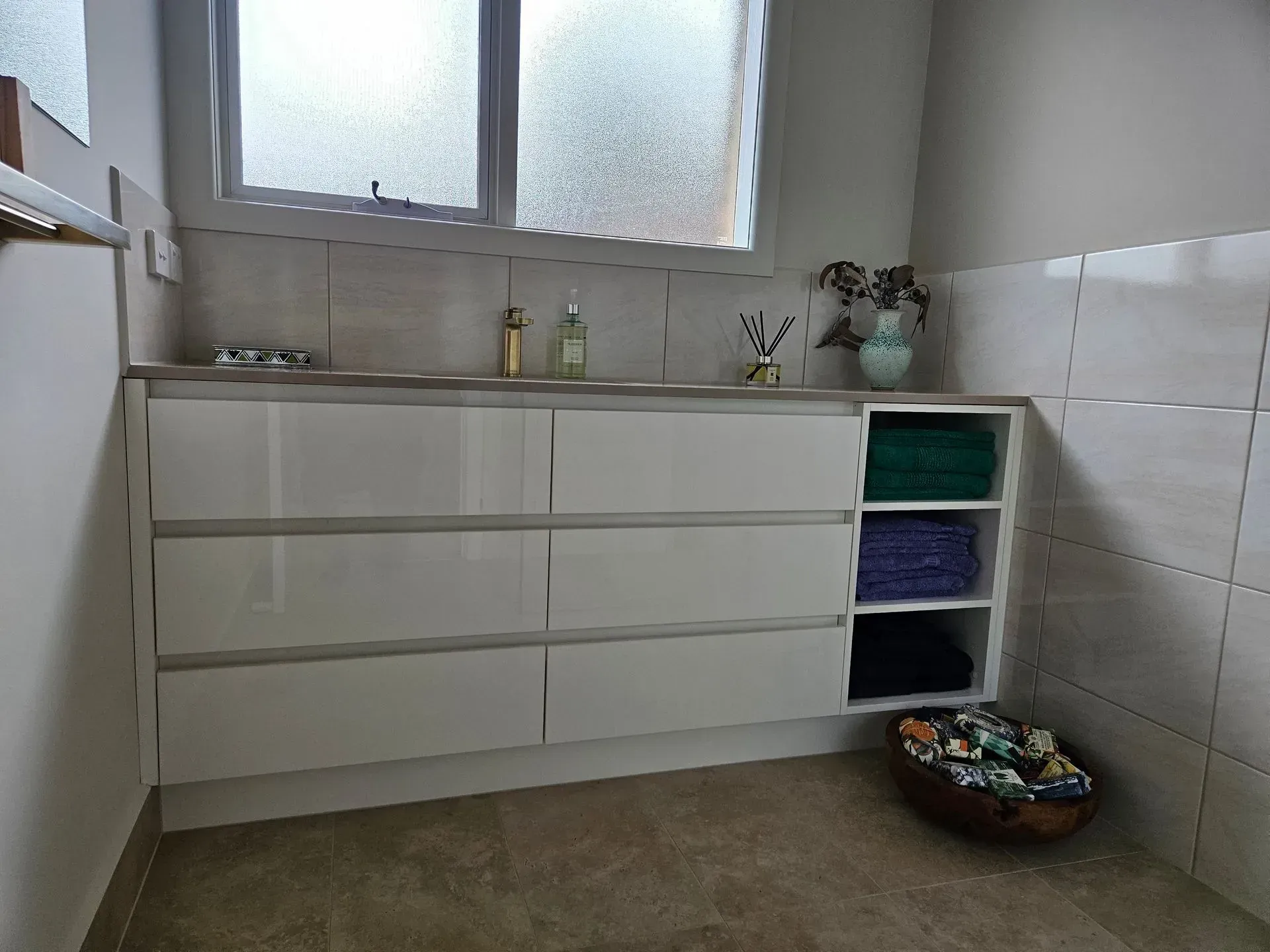Minimal kitchen with white drawers, tiled walls, frosted window, and baskets on the floor