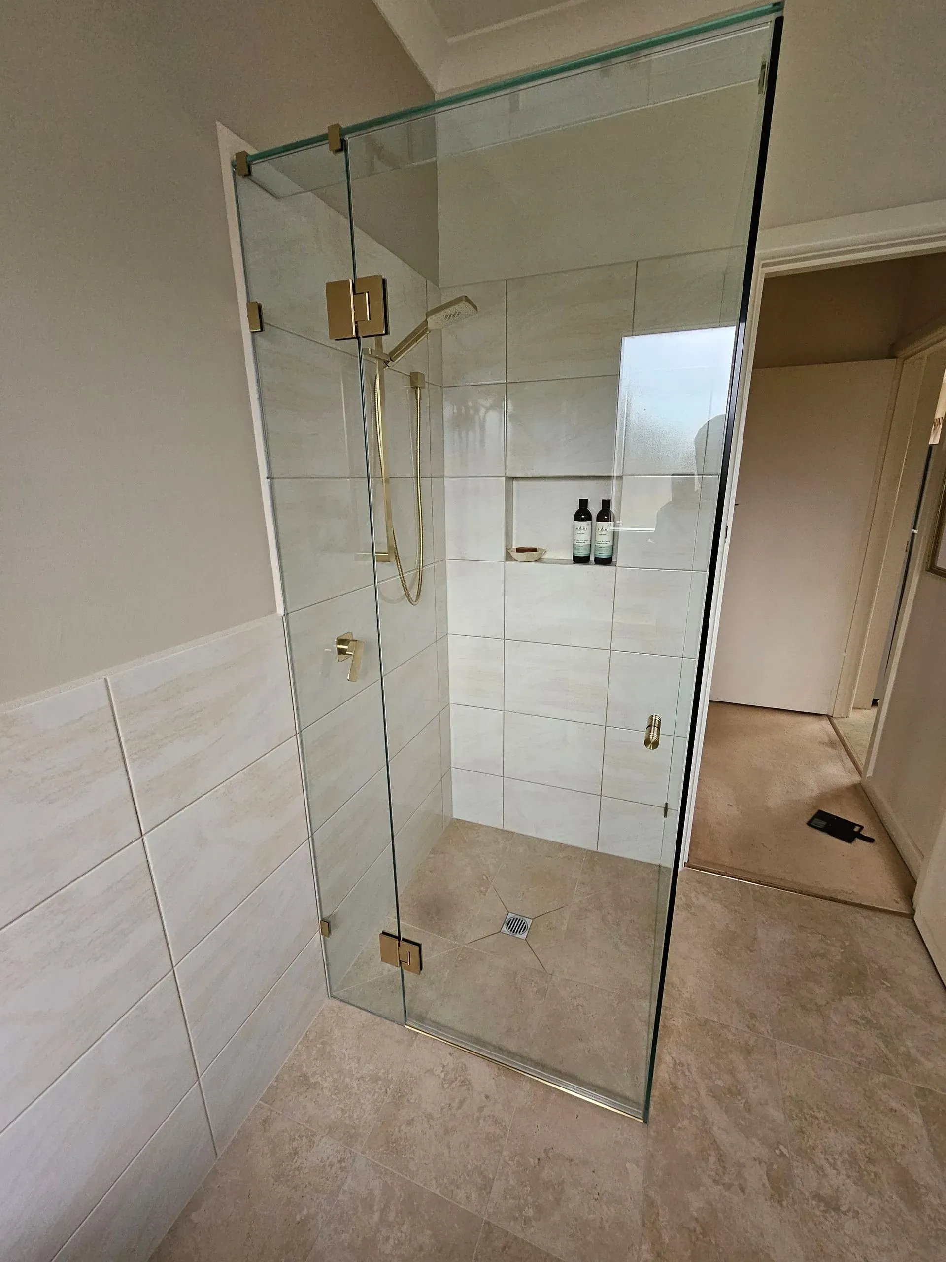 Glass shower enclosure in a tiled bathroom with beige carpet and a chrome shower fixture