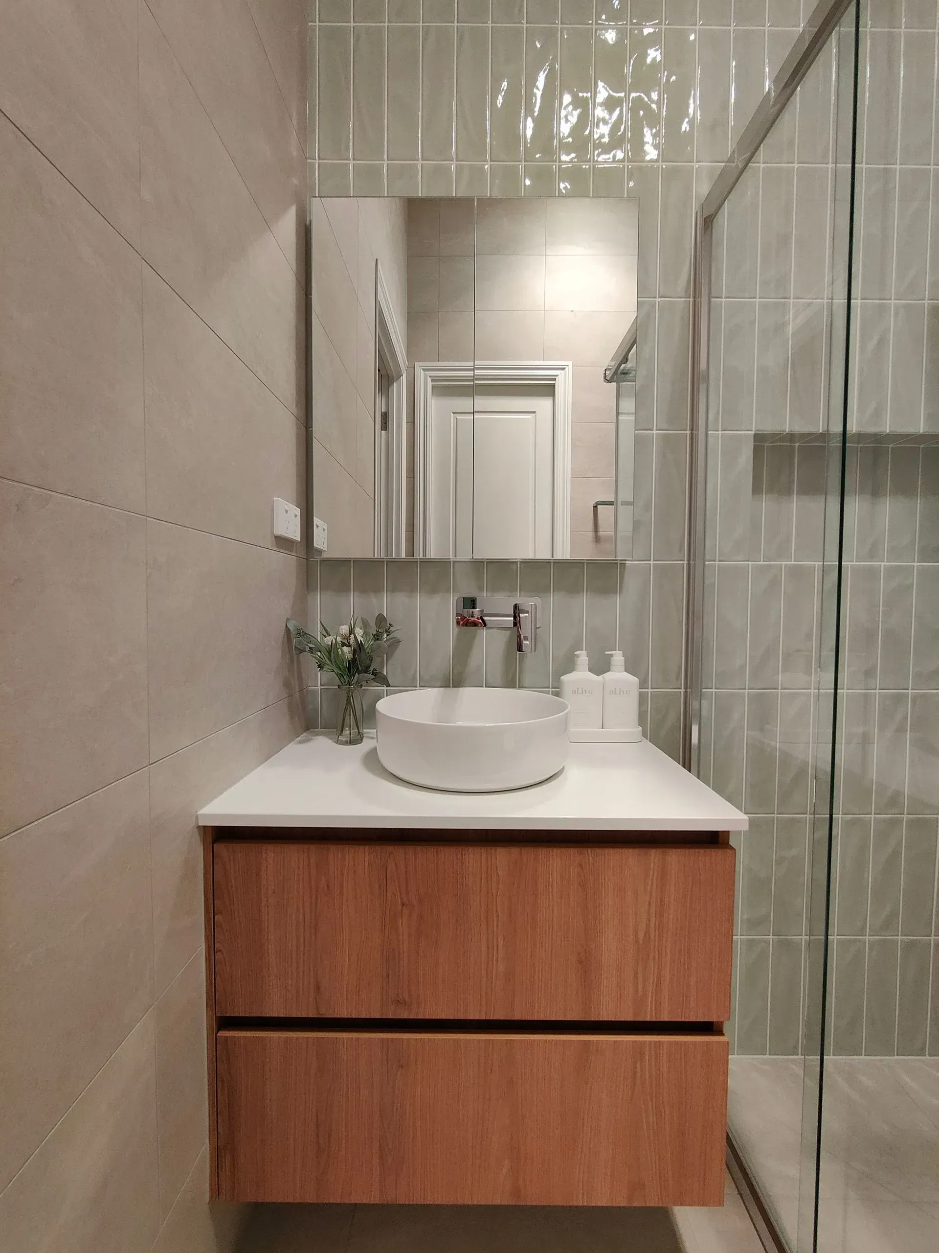 Modern bathroom vanity with round sink, wood drawers, mirror, and glass shower wall