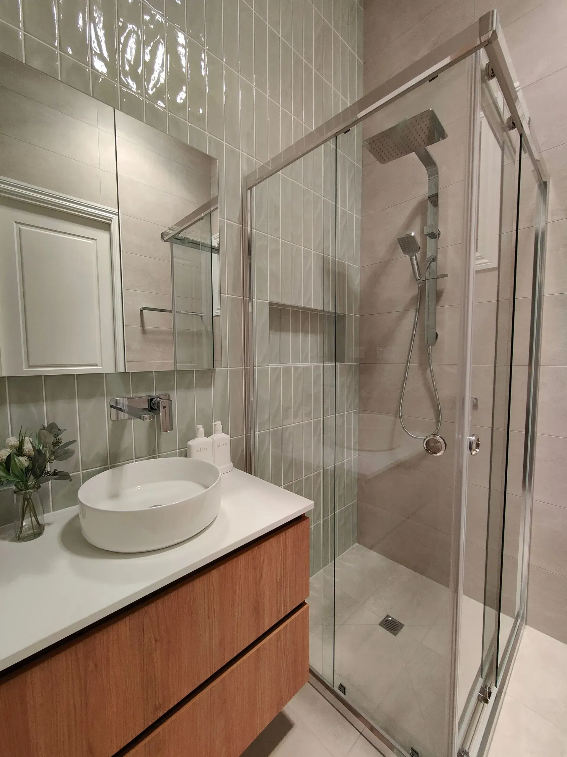 Modern bathroom with vanity sink, mirror, and glass shower enclosure on a neutral tiled wall.