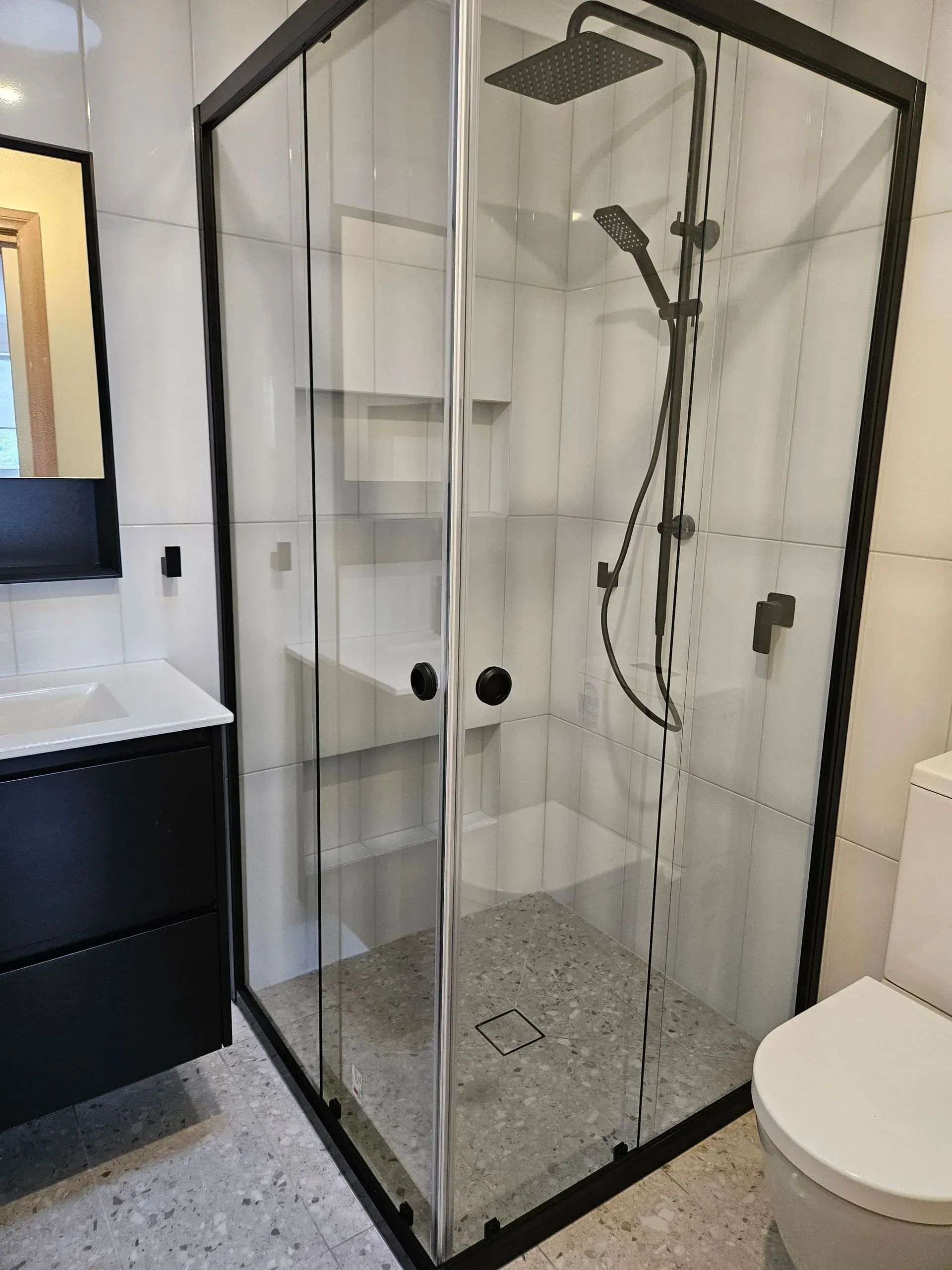 Small tiled bathroom with a glass corner shower enclosure beside a sink and toilet