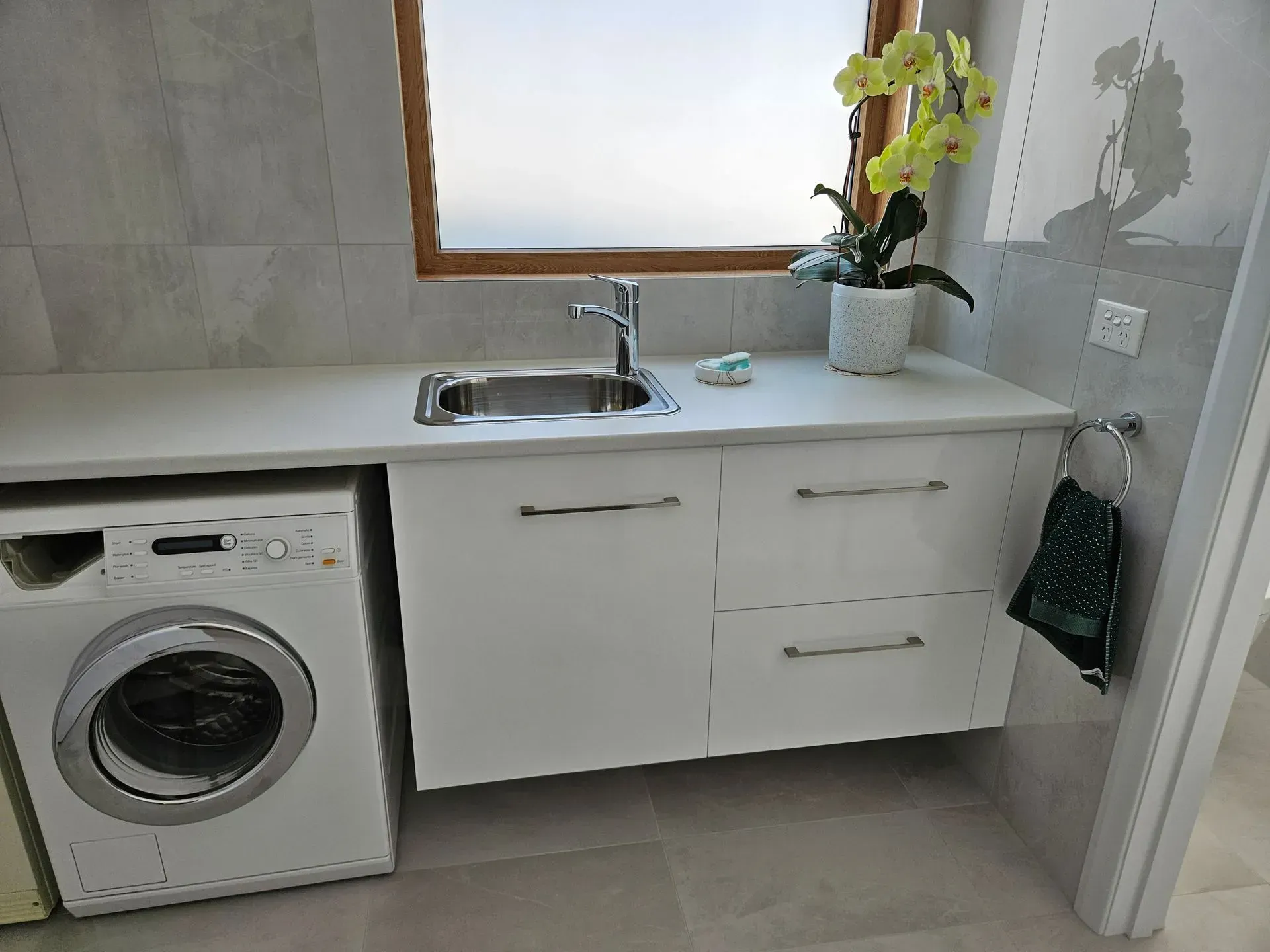 Laundry room sink with white cabinets, a washing machine, and a potted orchid on the counter.