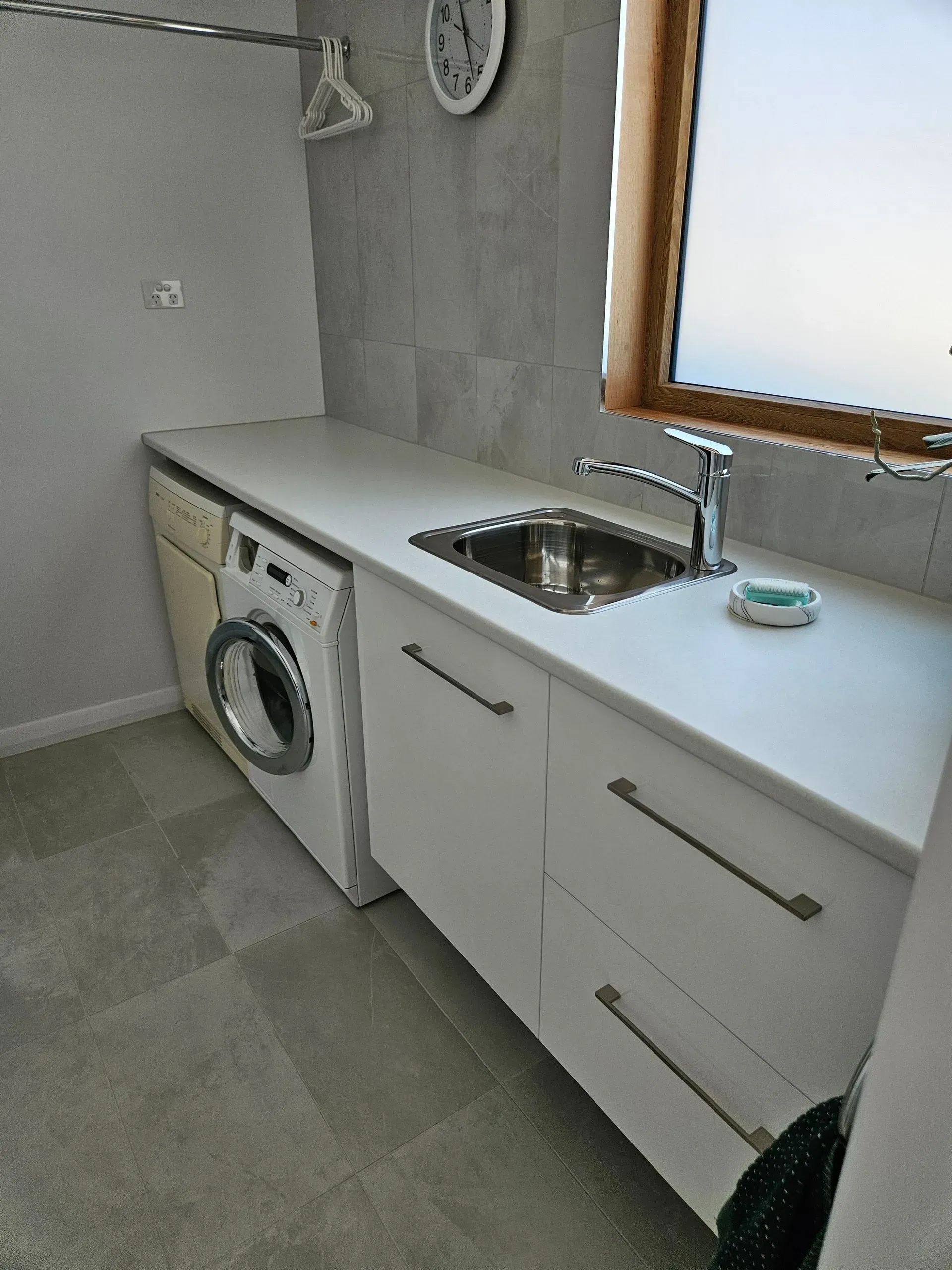 Modern kitchen countertop with sink, washing machine, white cabinets, and a window.