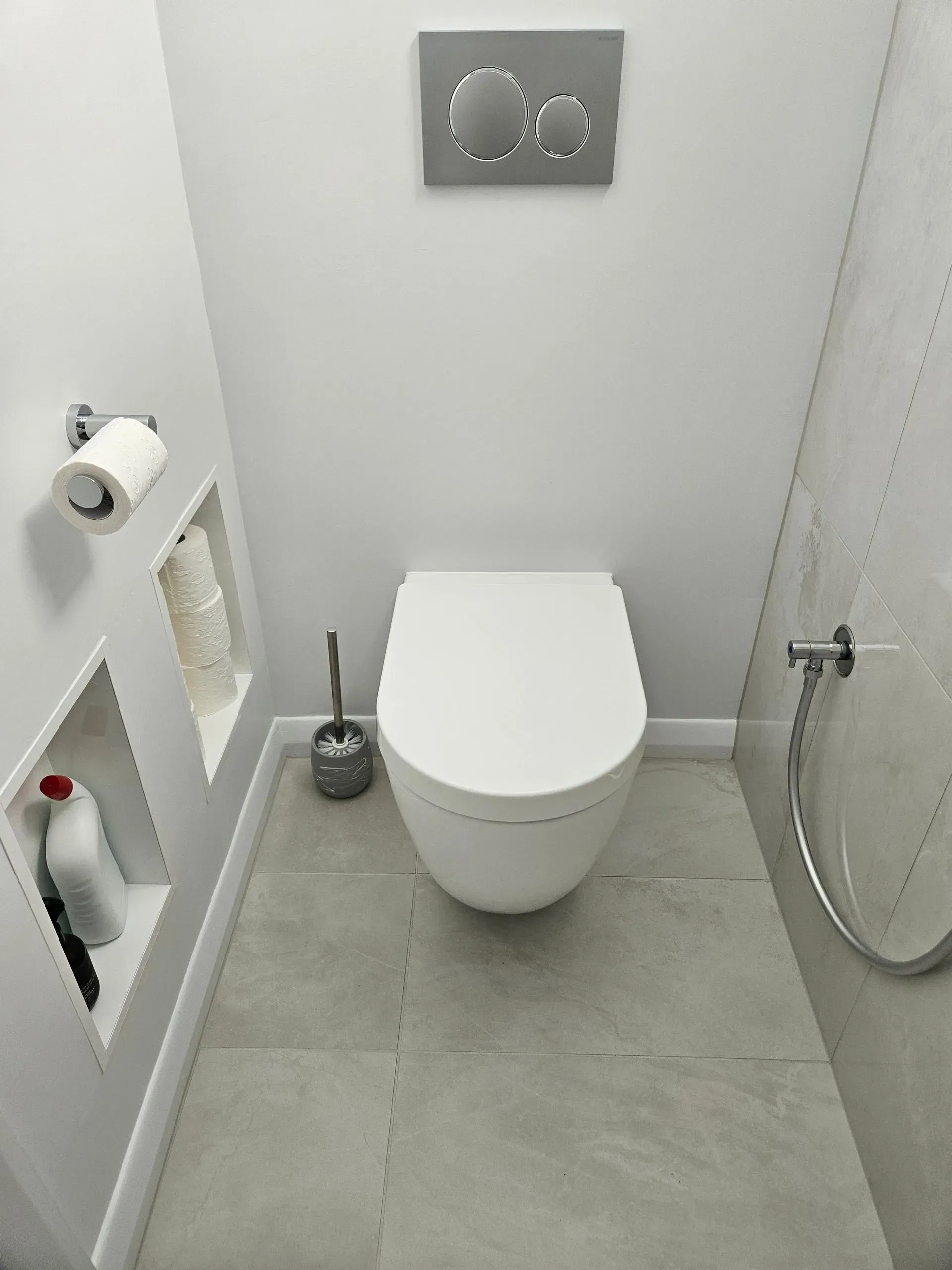 Small white bathroom with toilet, shower, toilet paper holder, and trash bin.