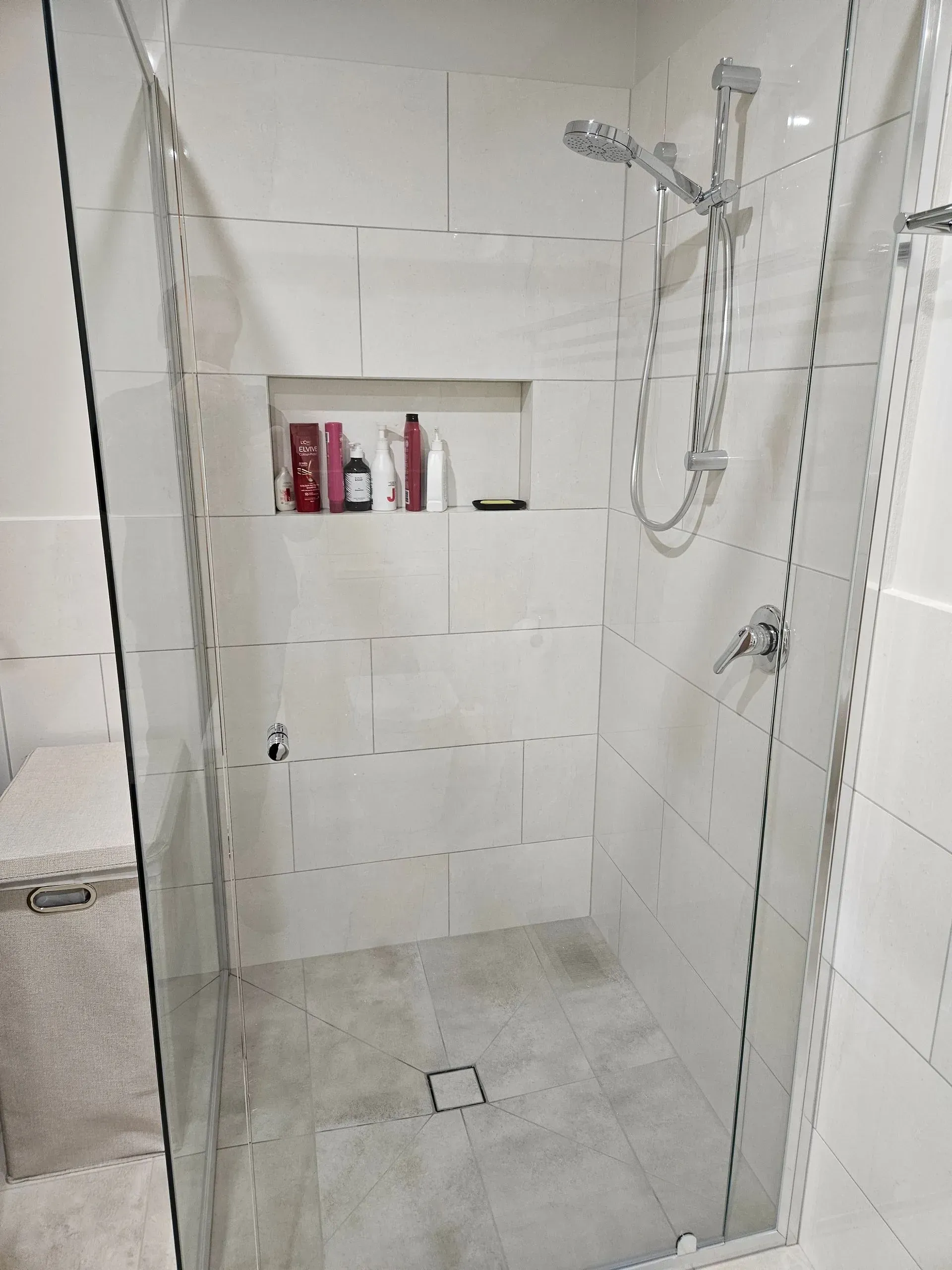 Glass shower with white tile, wall niche, and handheld showerhead with hose