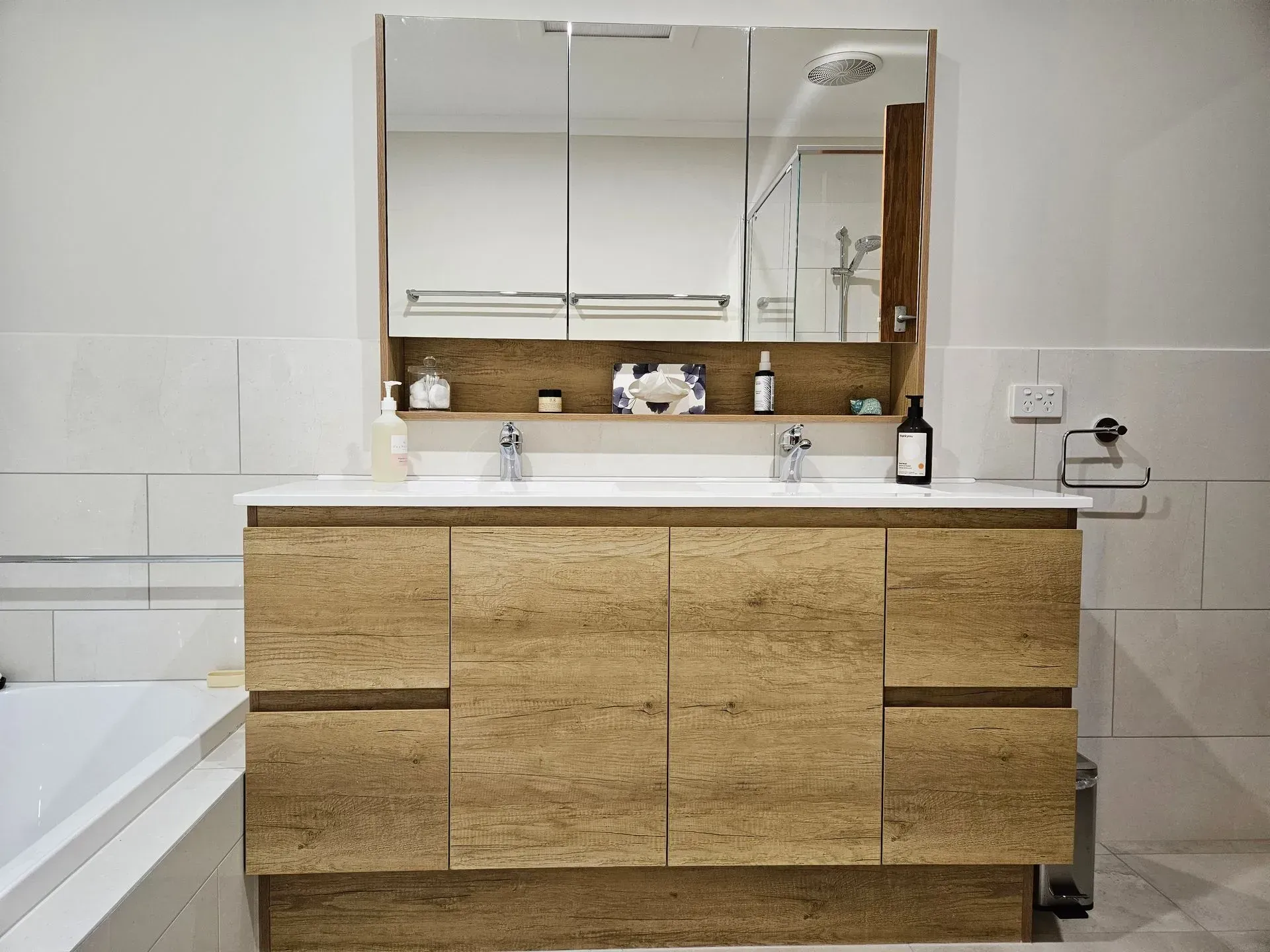 Modern bathroom with wood vanity, large mirror, white sink, and bathtub on the left