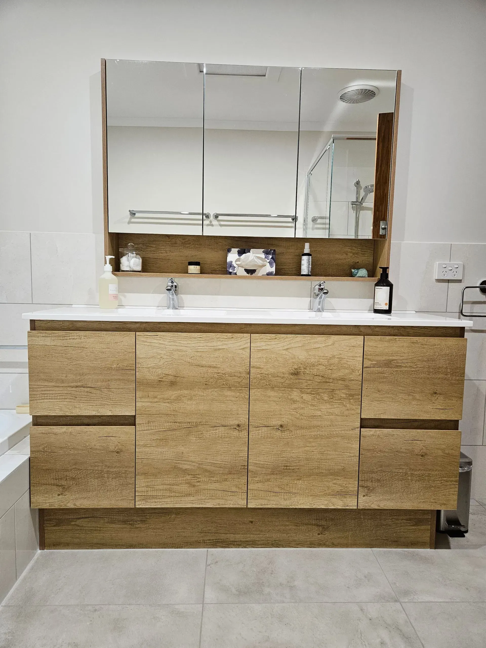 Modern bathroom vanity with wood cabinets, mirrored medicine cabinet, and white countertop sinks