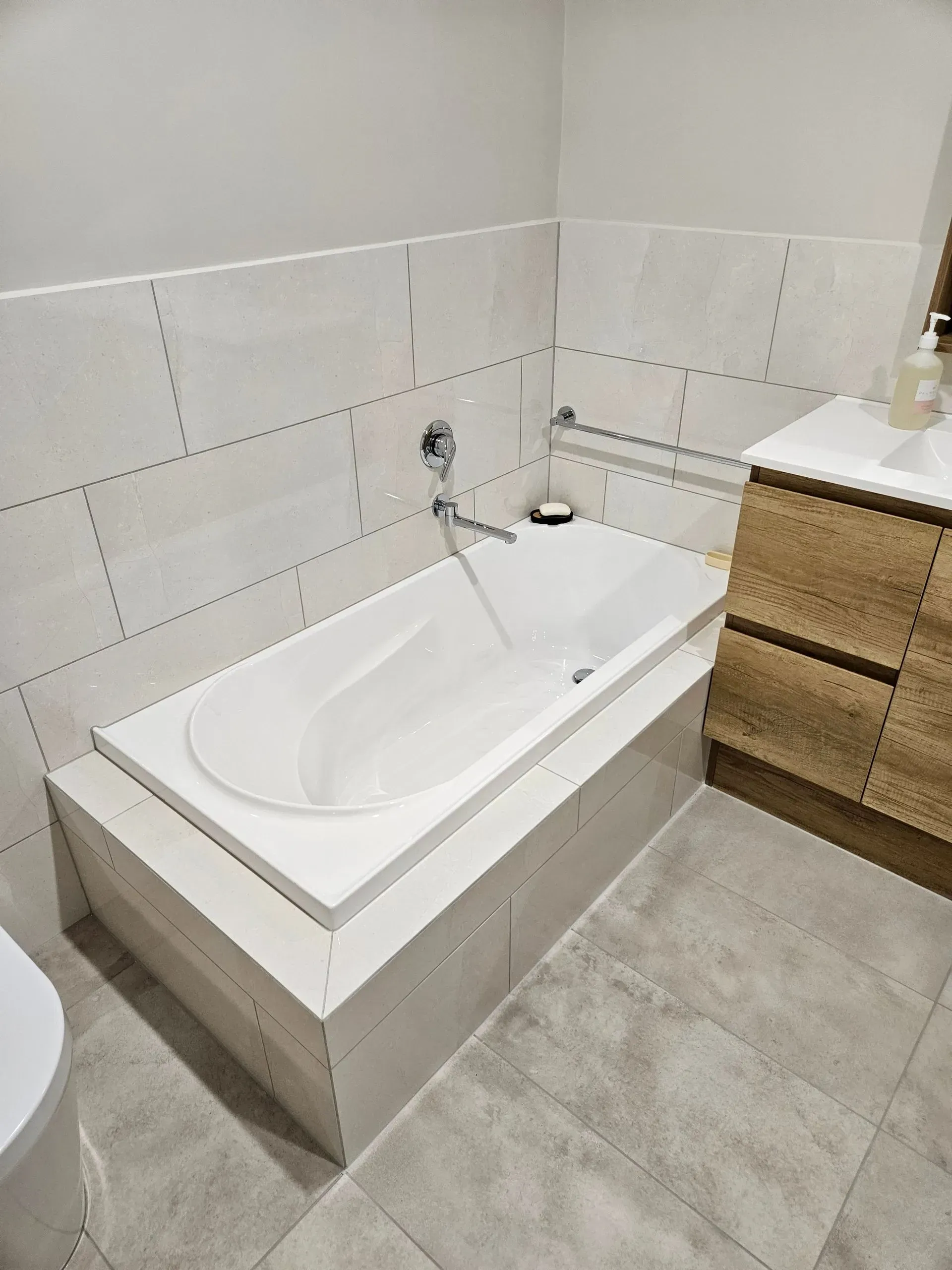Modern bathroom with a white bathtub, gray tile floor, and wood vanity counter