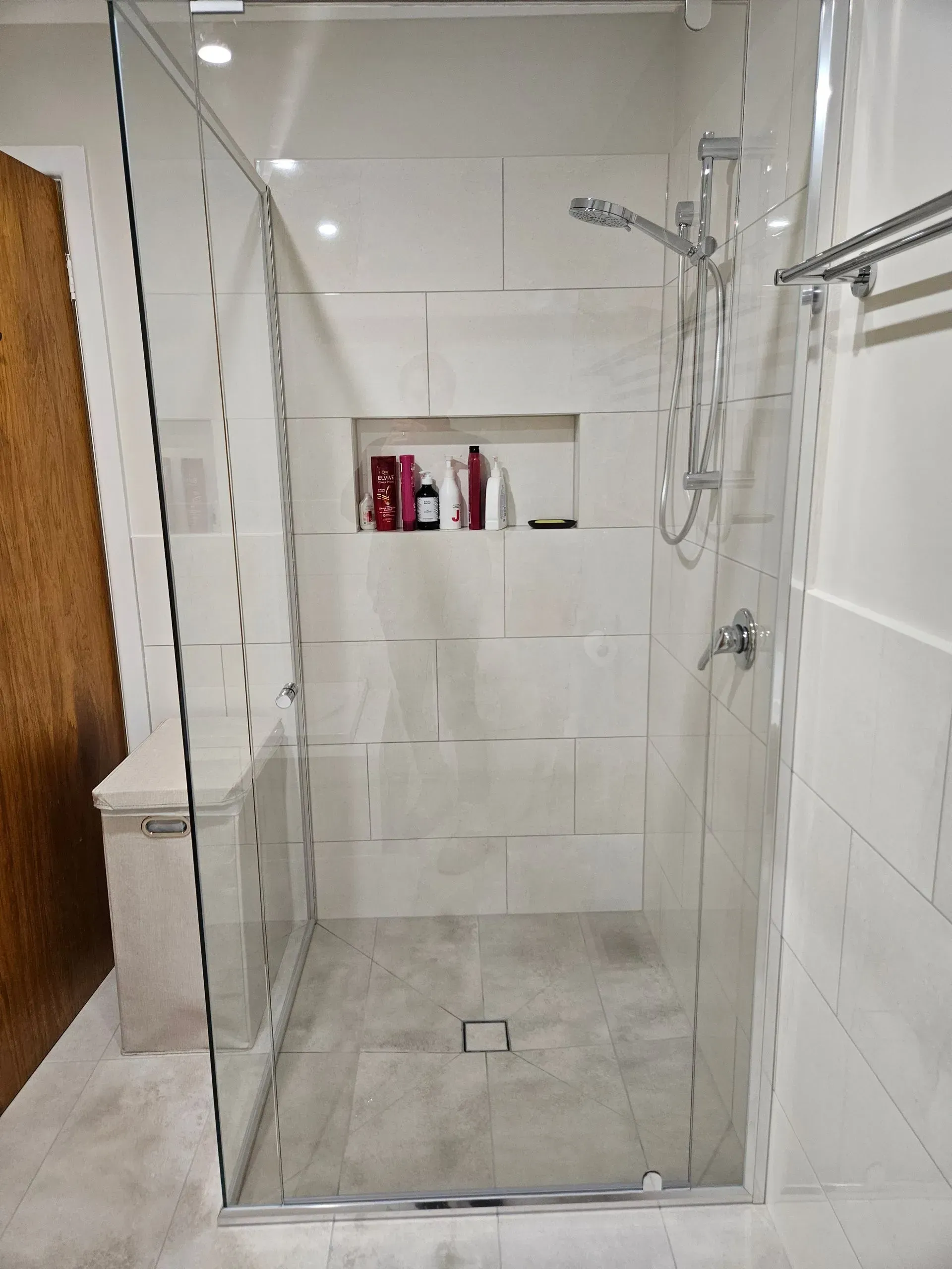 Glass shower stall with white tile walls and chrome fixtures in a bathroom