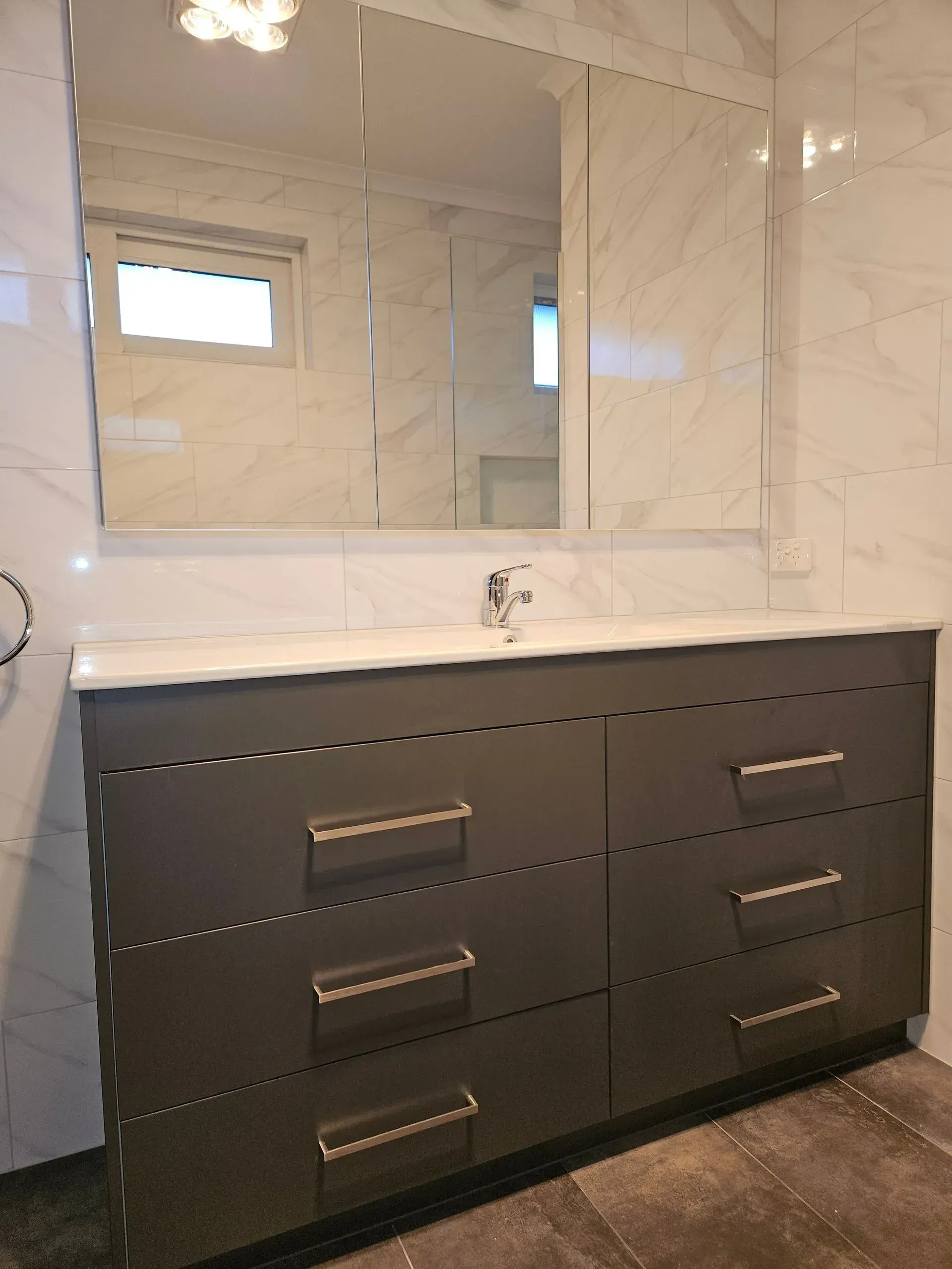 Modern bathroom vanity with dark drawers, marble countertop, and mirrored cabinet above.