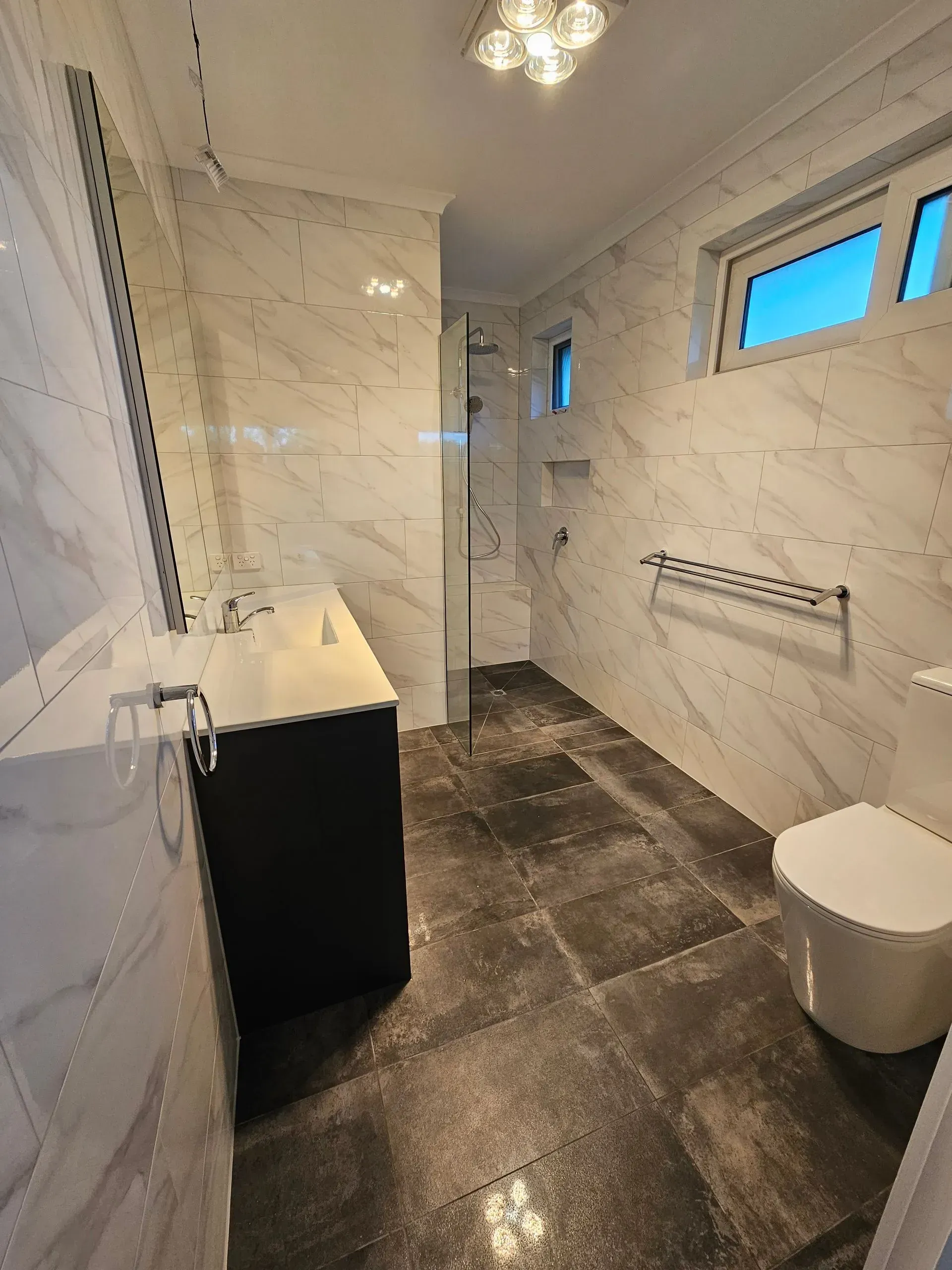 Modern marble bathroom with shower, vanity, toilet, and small frosted windows