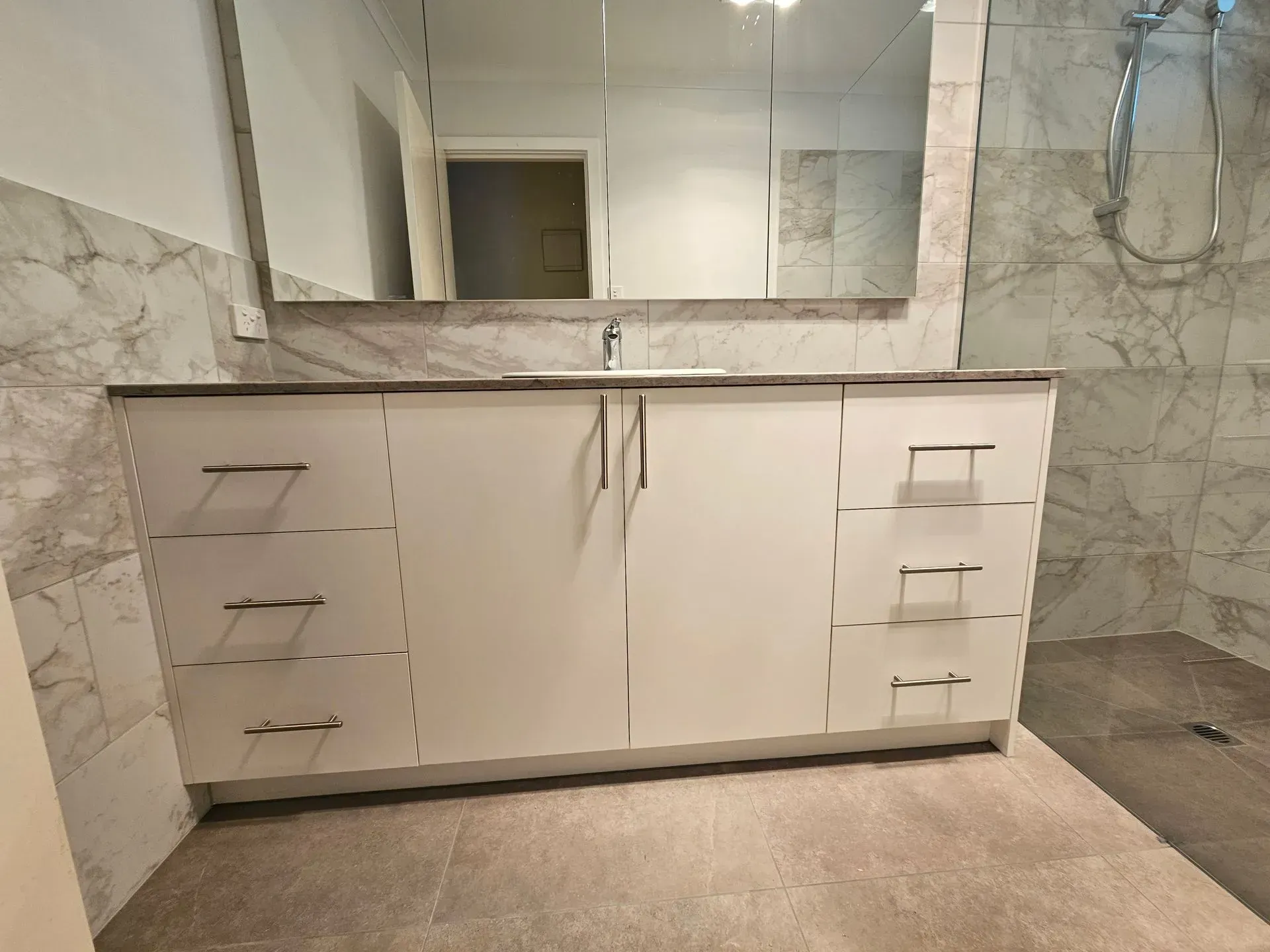 Modern bathroom vanity with white cabinets, marble walls, large mirror, and double sinks