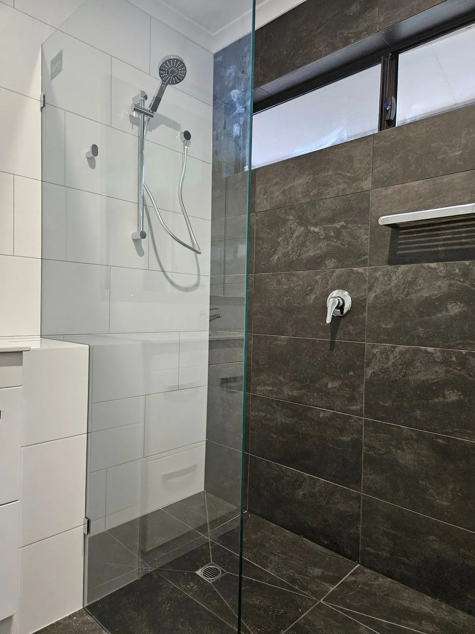 Modern bathroom shower with glass partition, white tile walls, dark stone tile, and a handheld showerhead